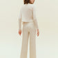 Back view of woman standing wearing off white knit pants with pockets with white knit cardigan