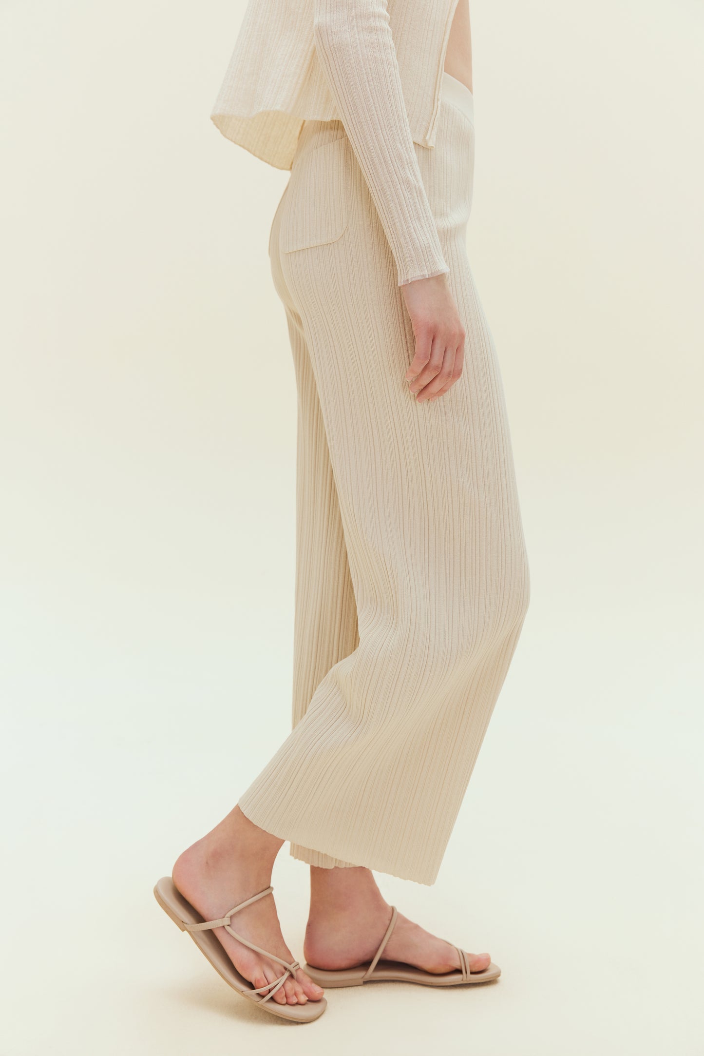Side view of woman standing wearing off white knit pants