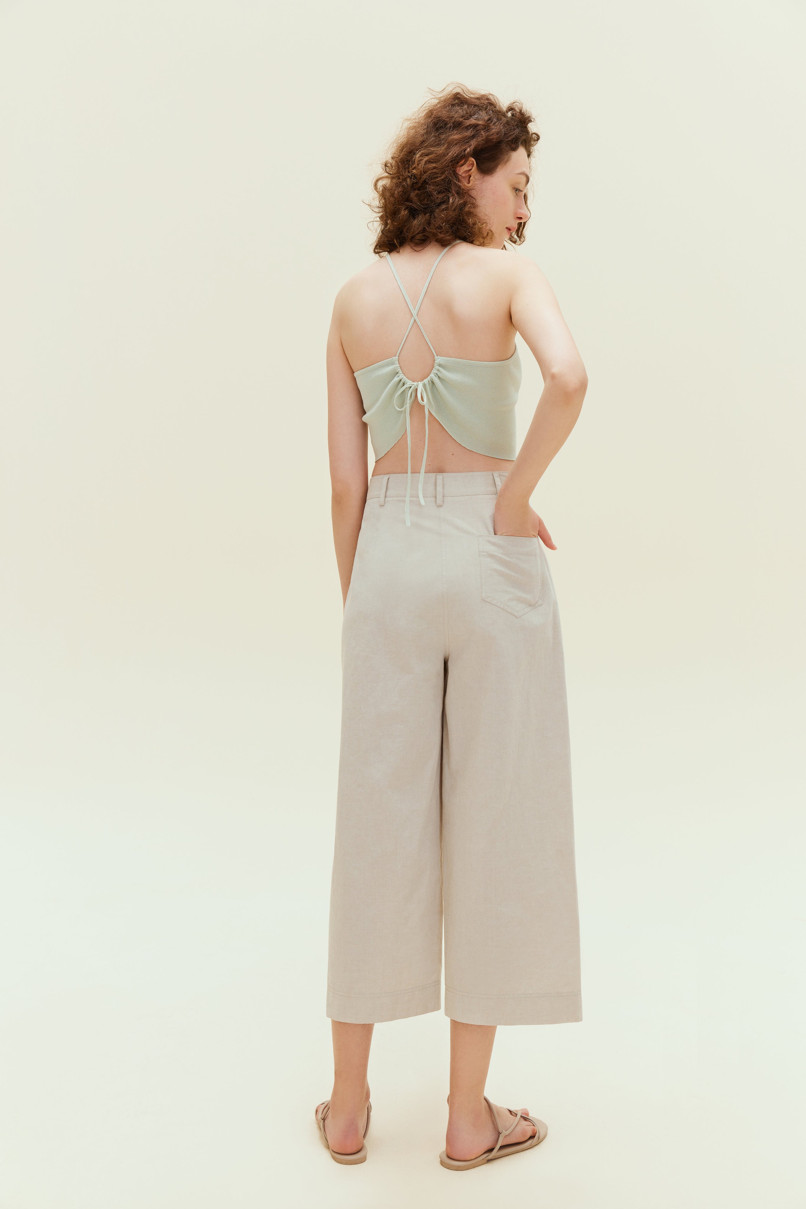 Back view of woman standing wearing light green colored tank top with khaki capris