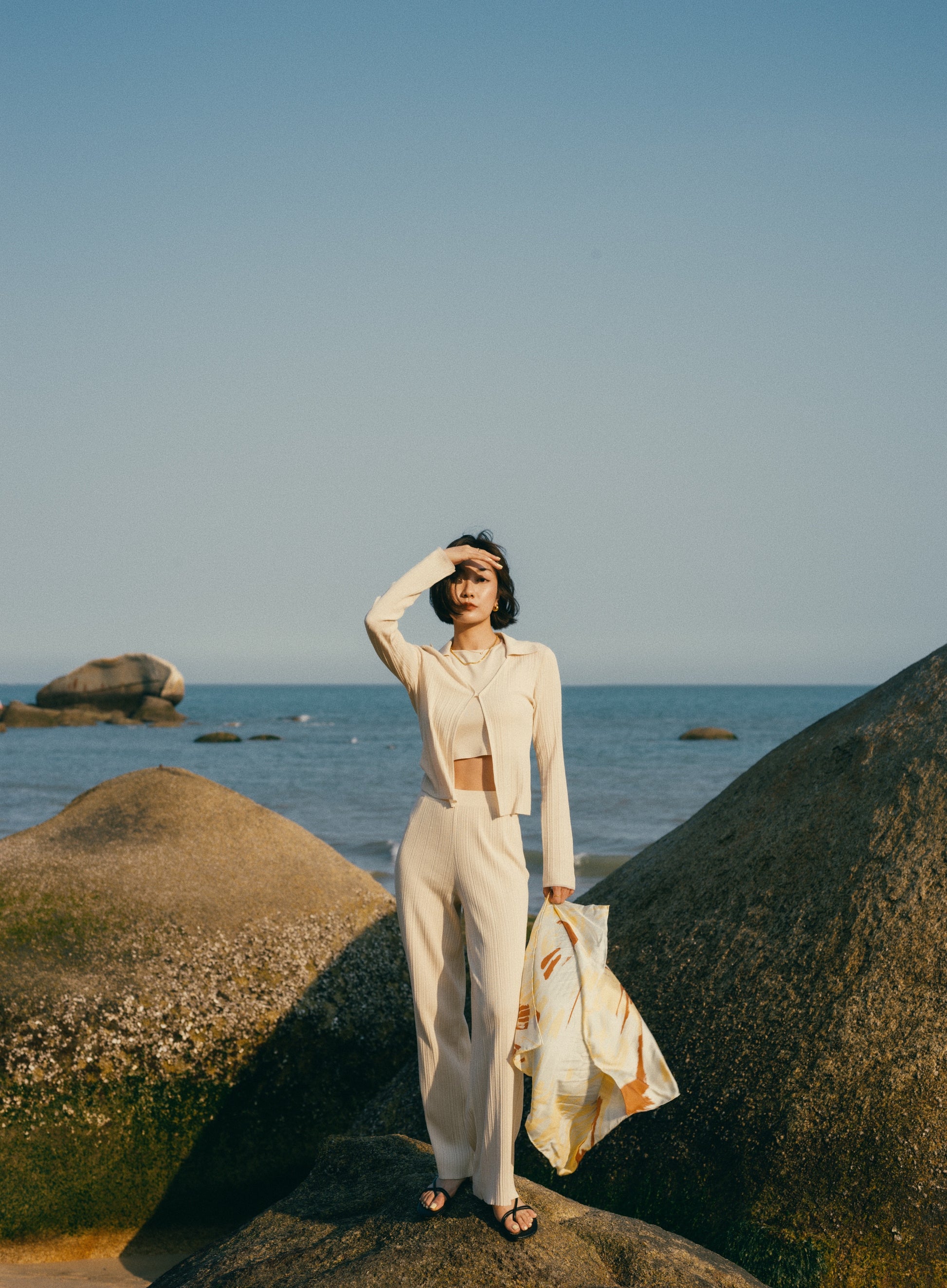 Woman by beach wearing off white knit cardigan with collar over matching tank top and pants