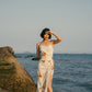Woman standing on beach wearing spaghetti strap dress with brown, beige, white print with high slit on side