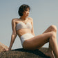 Woman sitting on rock wearing gold halter neck bikini bop and high waisted bikini bottom
