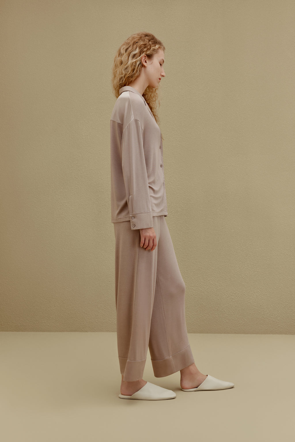 Side view of woman wearing tan button up pajama shirt with pocket and matching pajama pants