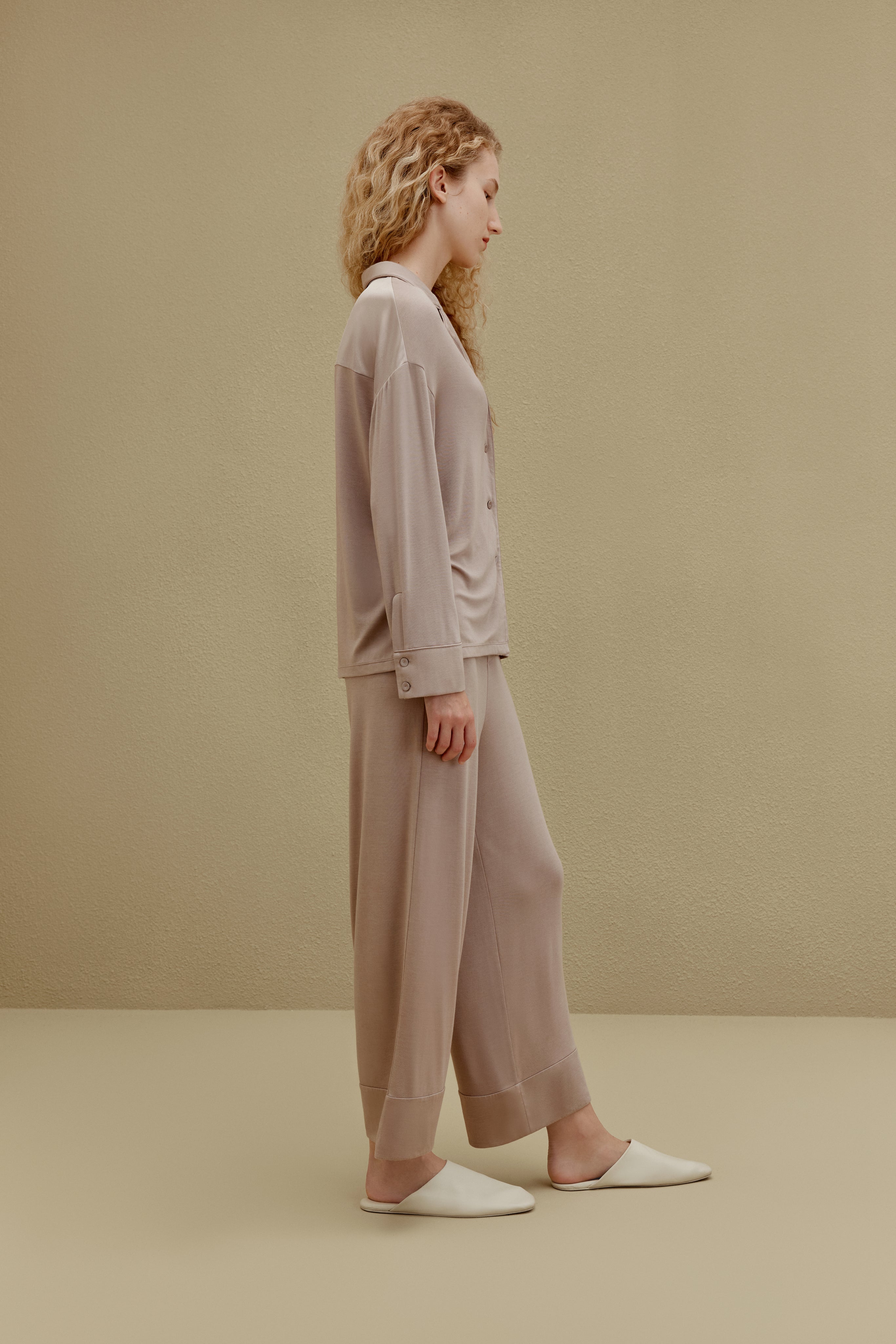 Side view of woman wearing tan button up pajama shirt with pocket and matching pajama pants