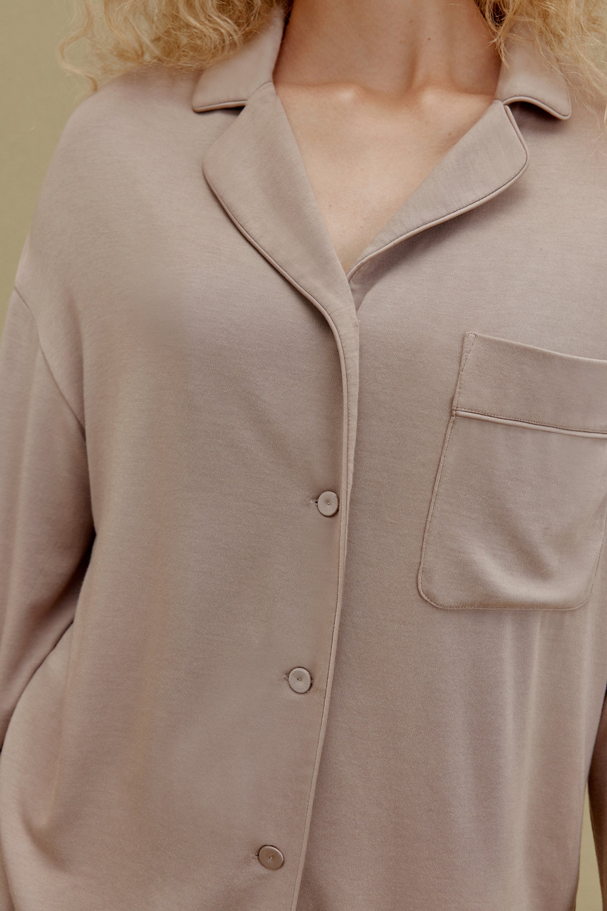 Close up front view of woman wearing tan button up pajama shirt with pocket