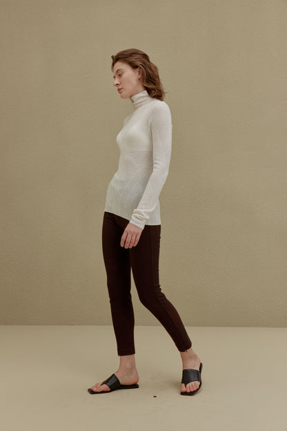 side of woman in white turtleneck sweater and brown pants