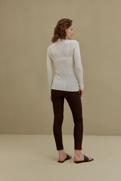 back of woman in white turtleneck sweater and brown pants