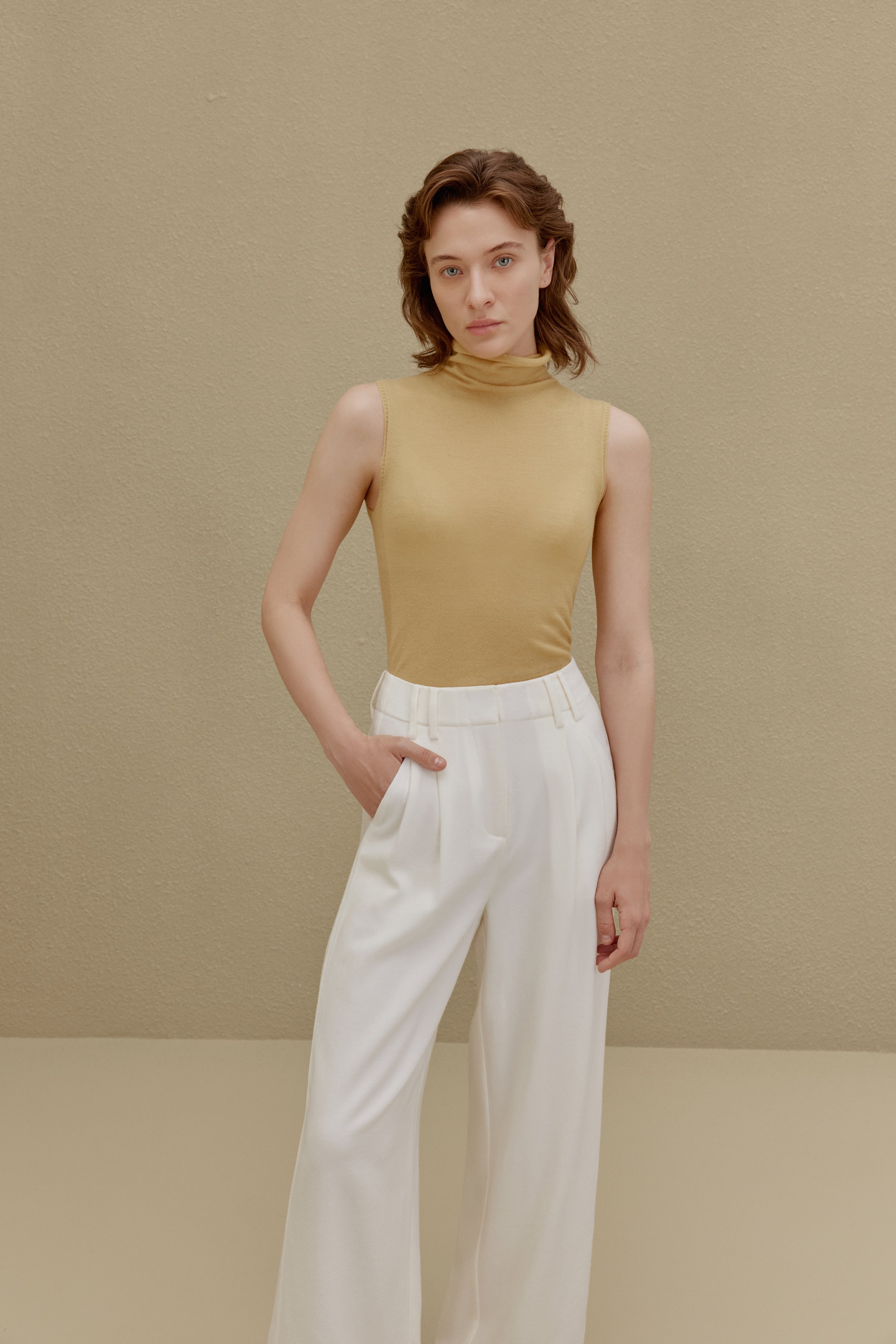 Woman in yellow knit turtle neck sleeveless top and white pants