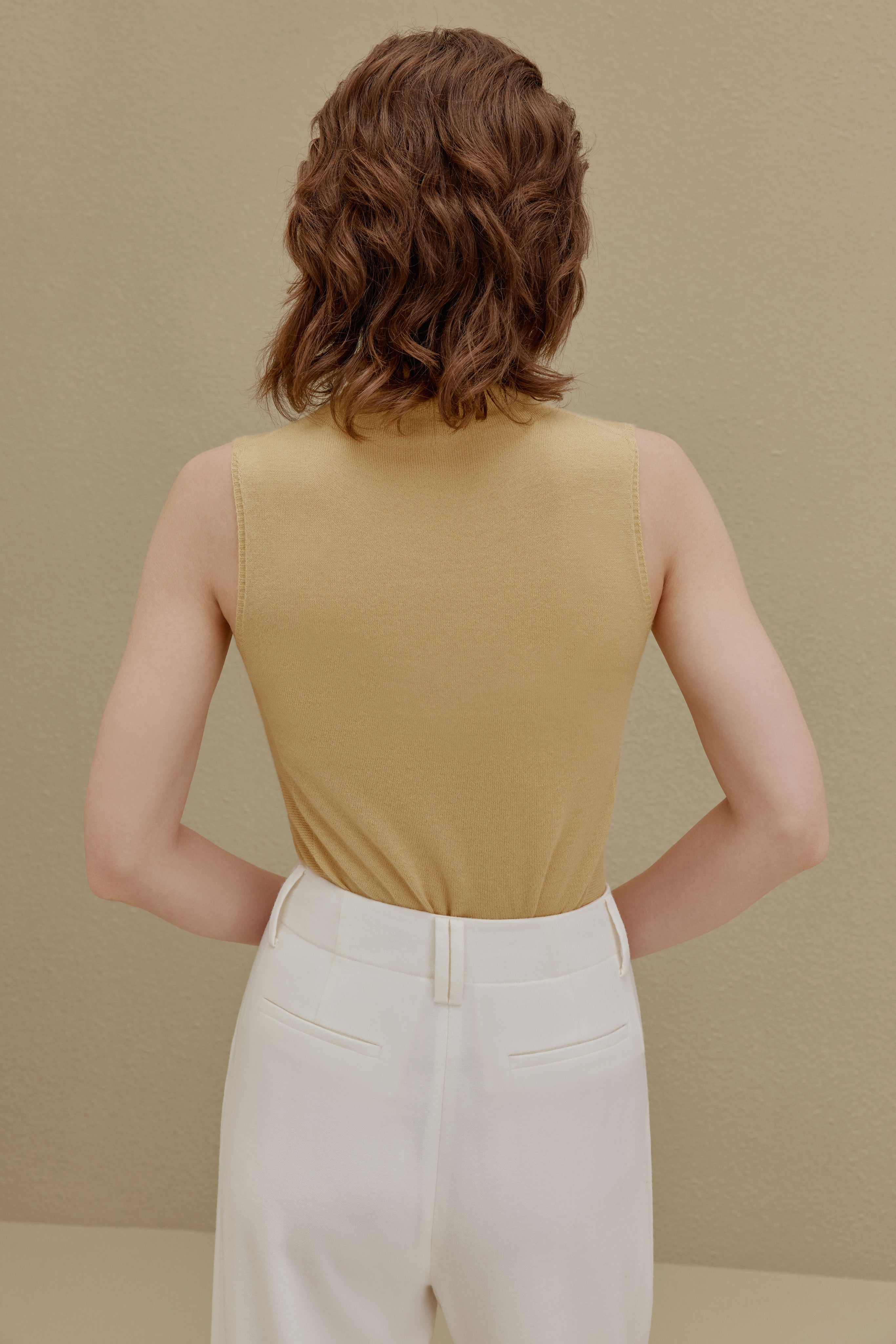 back of woman in yellow knit turtle neck sleeveless top