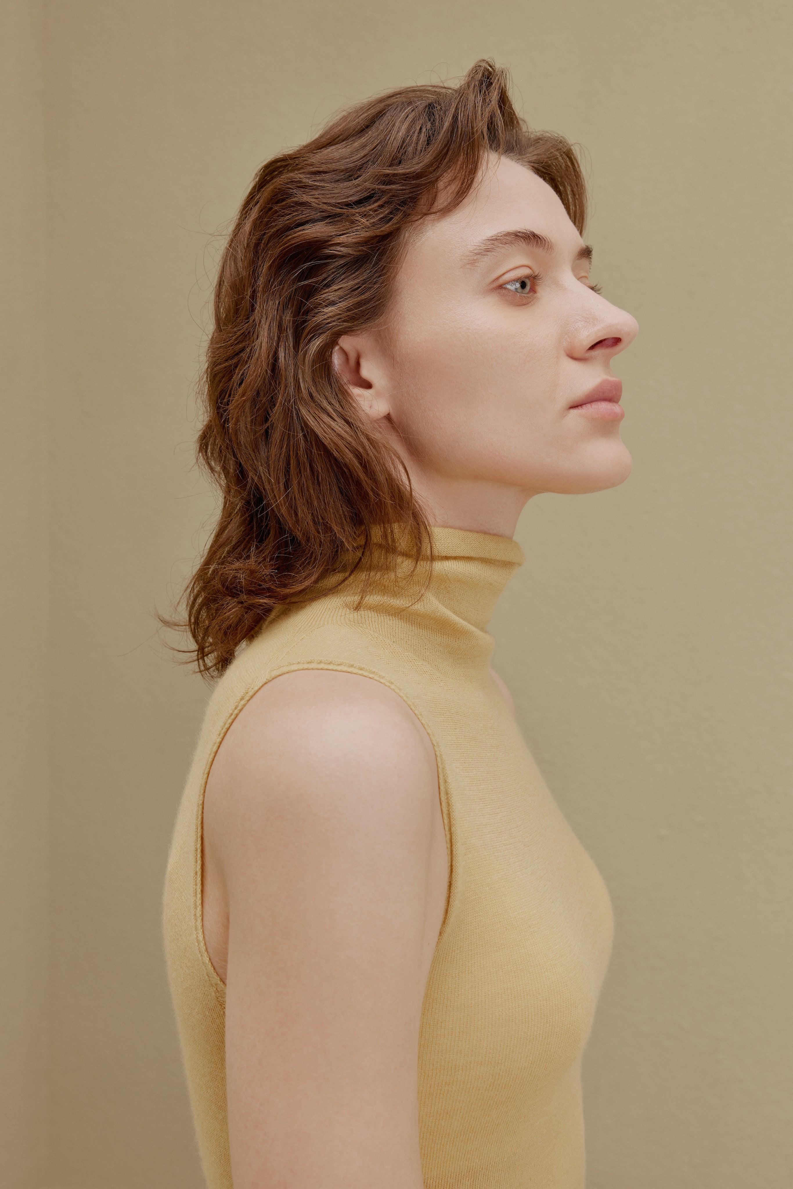 Side of woman in yellow knit turtle neck sleeveless top