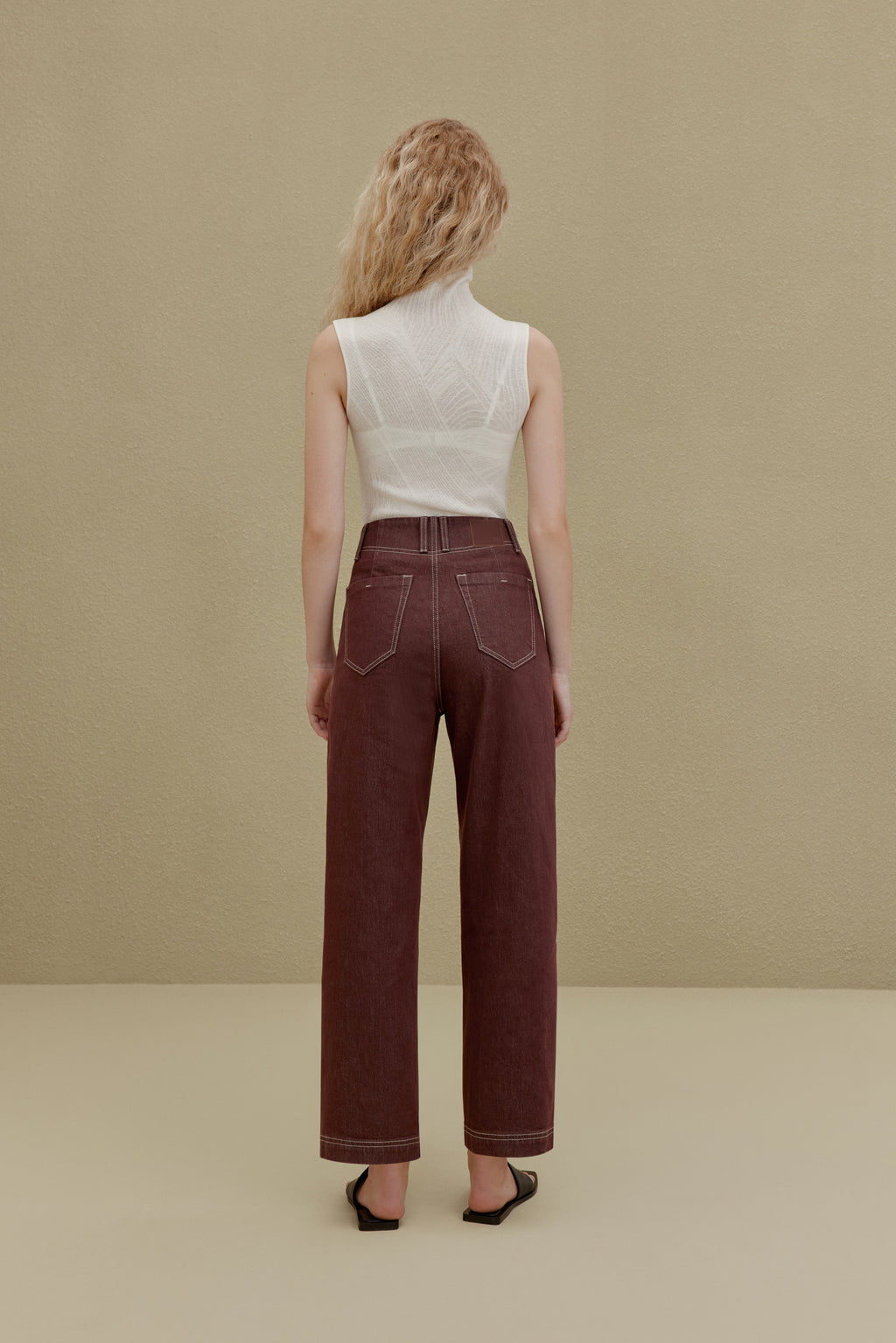 back of woman in white sleeveless top and brown pants
