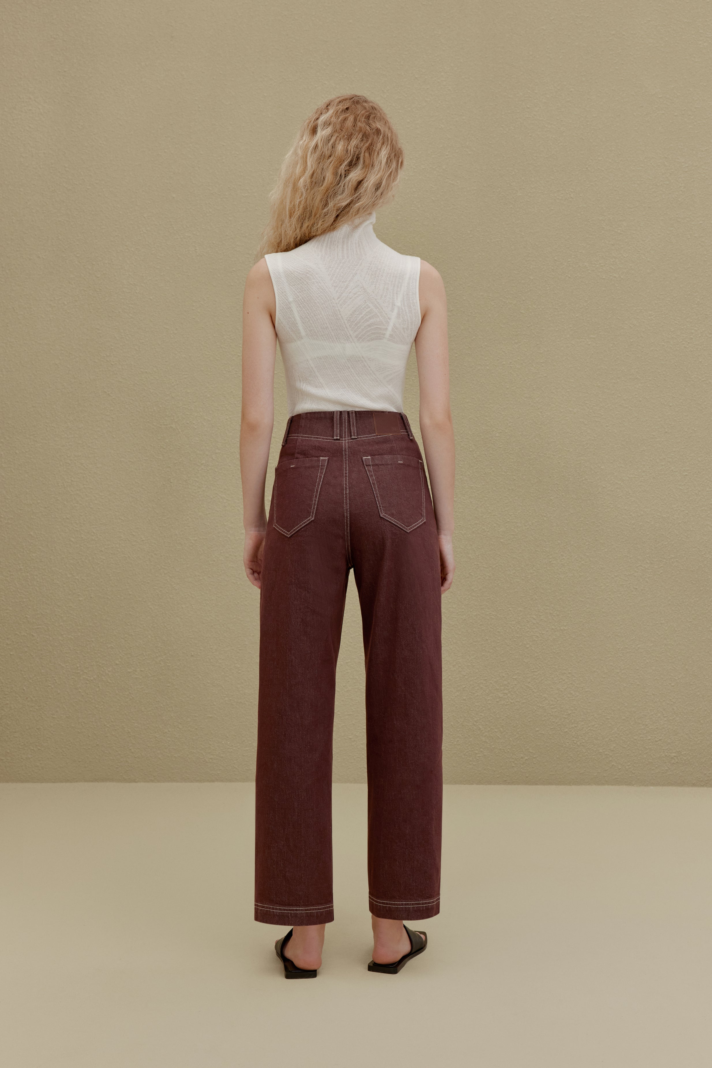 back of woman in white sleeveless top and brown pants