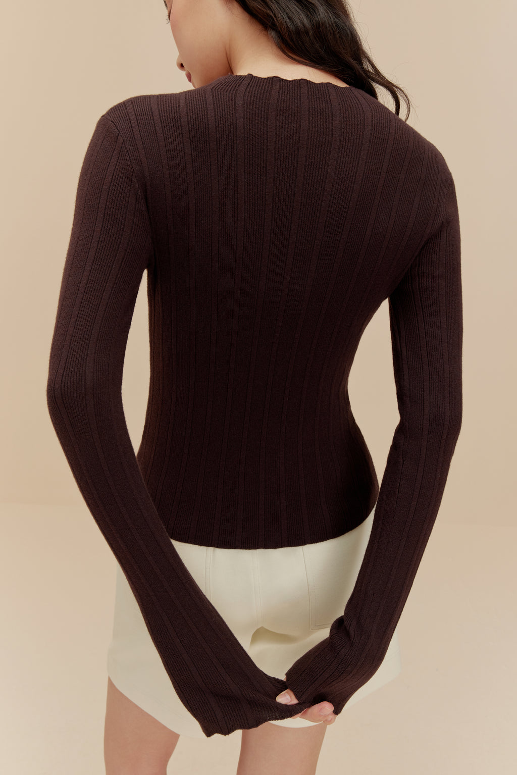 back of woman in brown sweater and white shorts