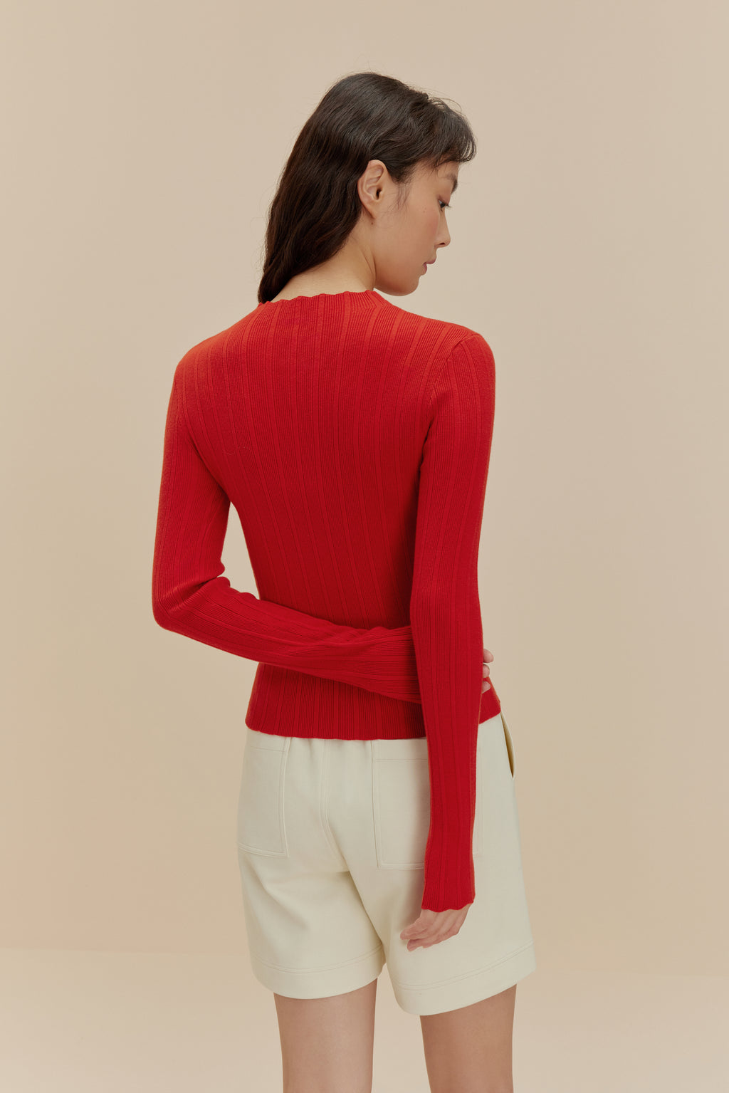 back of woman in red sweater  and white shorts
