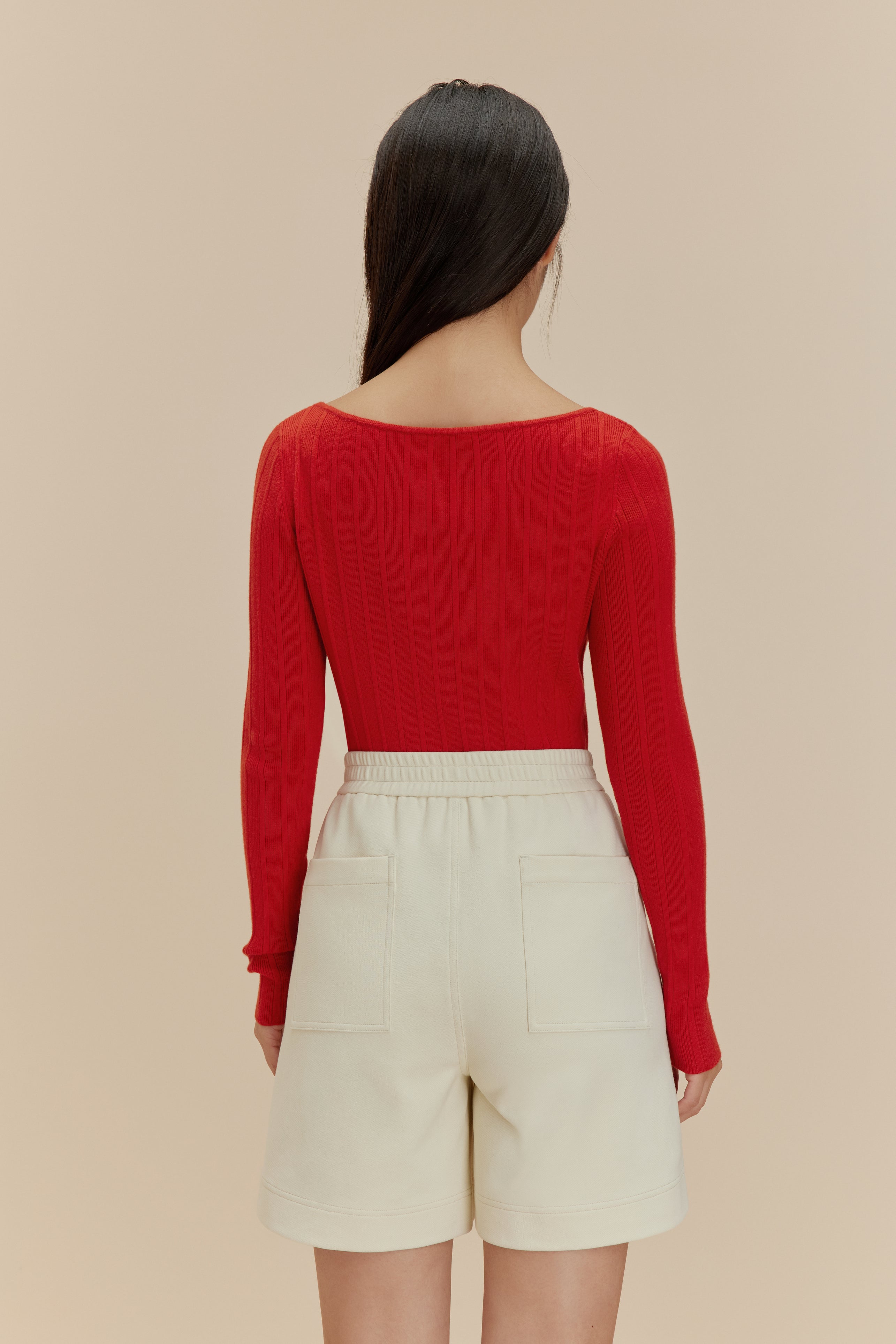 back of woman in red cardigan and white shorts