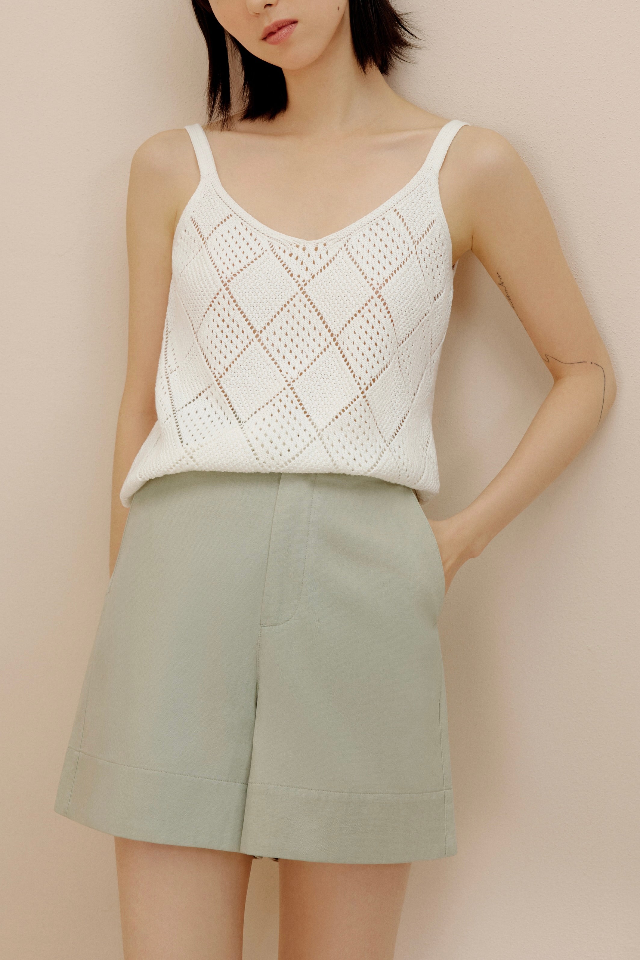 Woman wearing cream crochet tank top with green shorts.