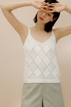 Woman stretching arms wearing cream crochet tank top with green shorts.