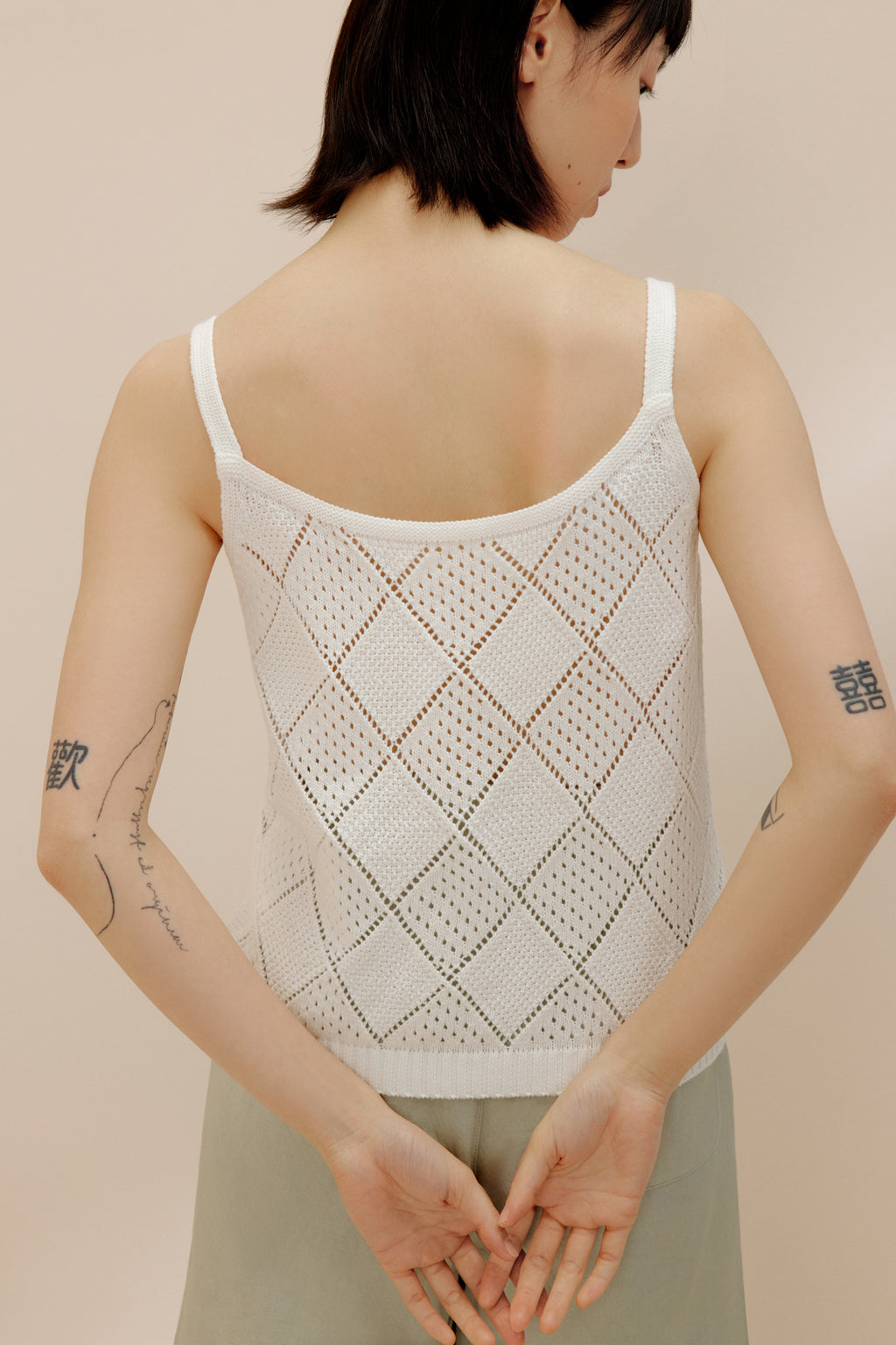 Back view of woman wearing cream crochet tank top with green shorts.