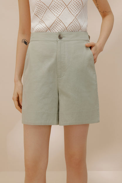 Front view of model putting her hand into pocket of green shorts.