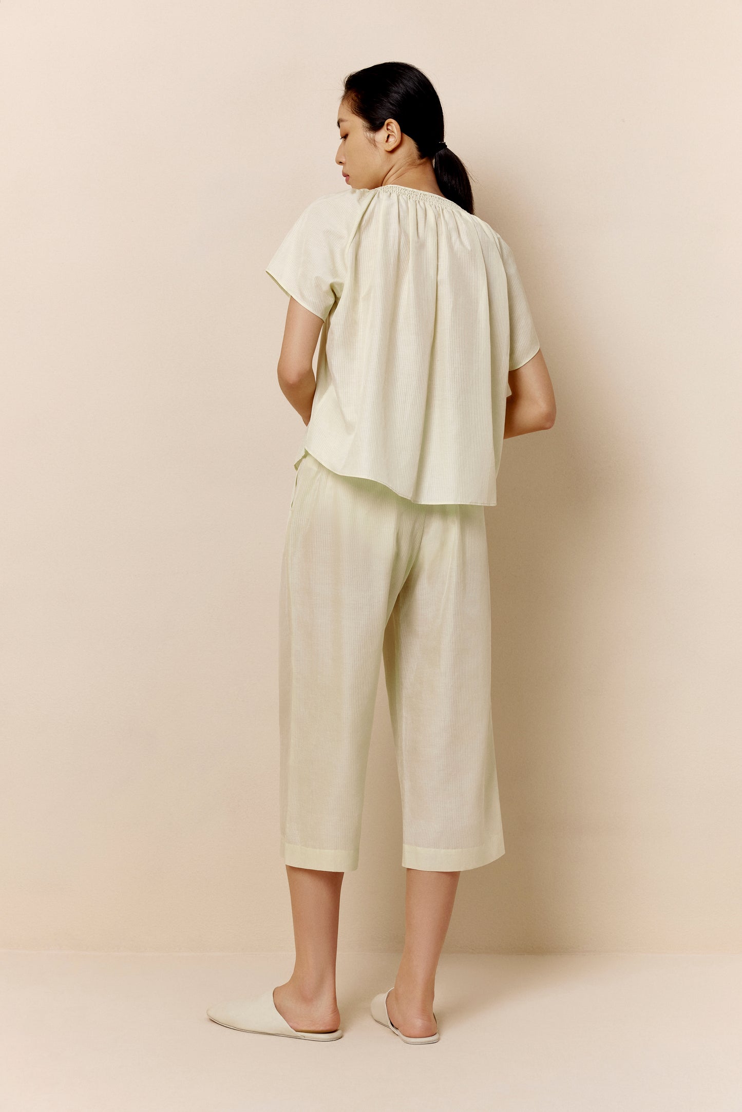 A woman wears off-white pajamas from back.