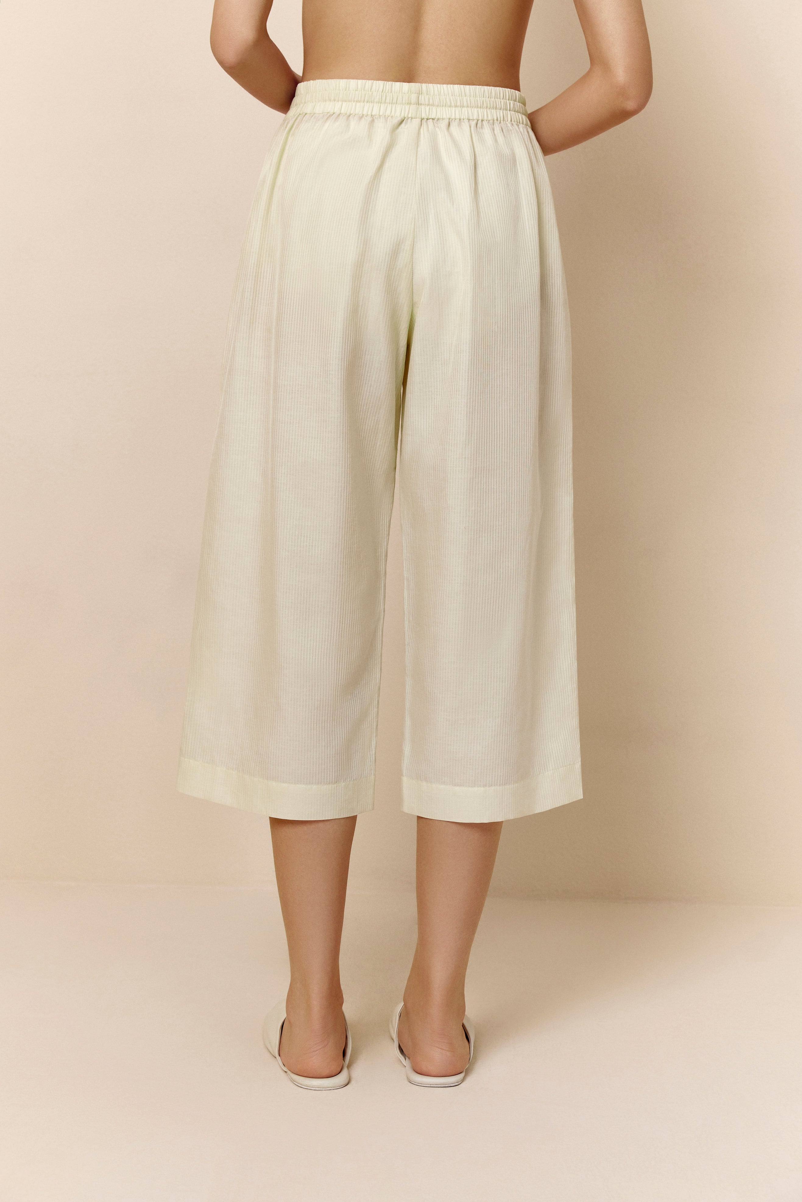 Back of bottom half of woman wearing off-white cropped pajama pants