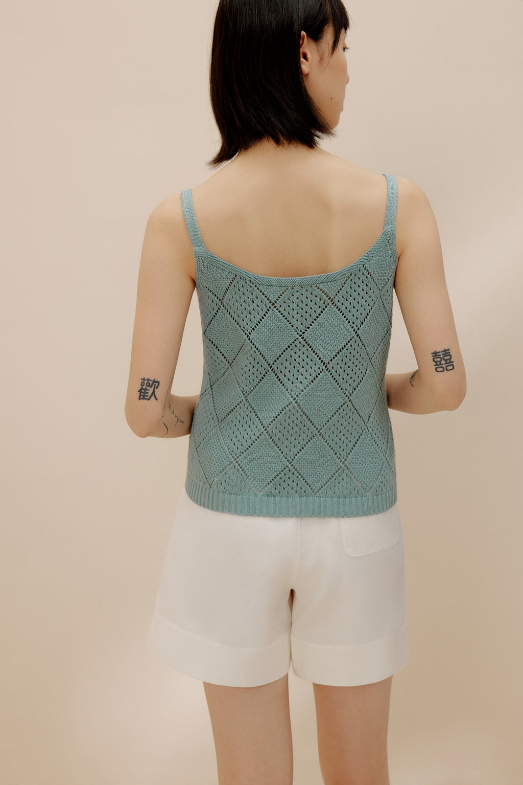 Back view of woman wearing blue crochet tank top with white shorts.