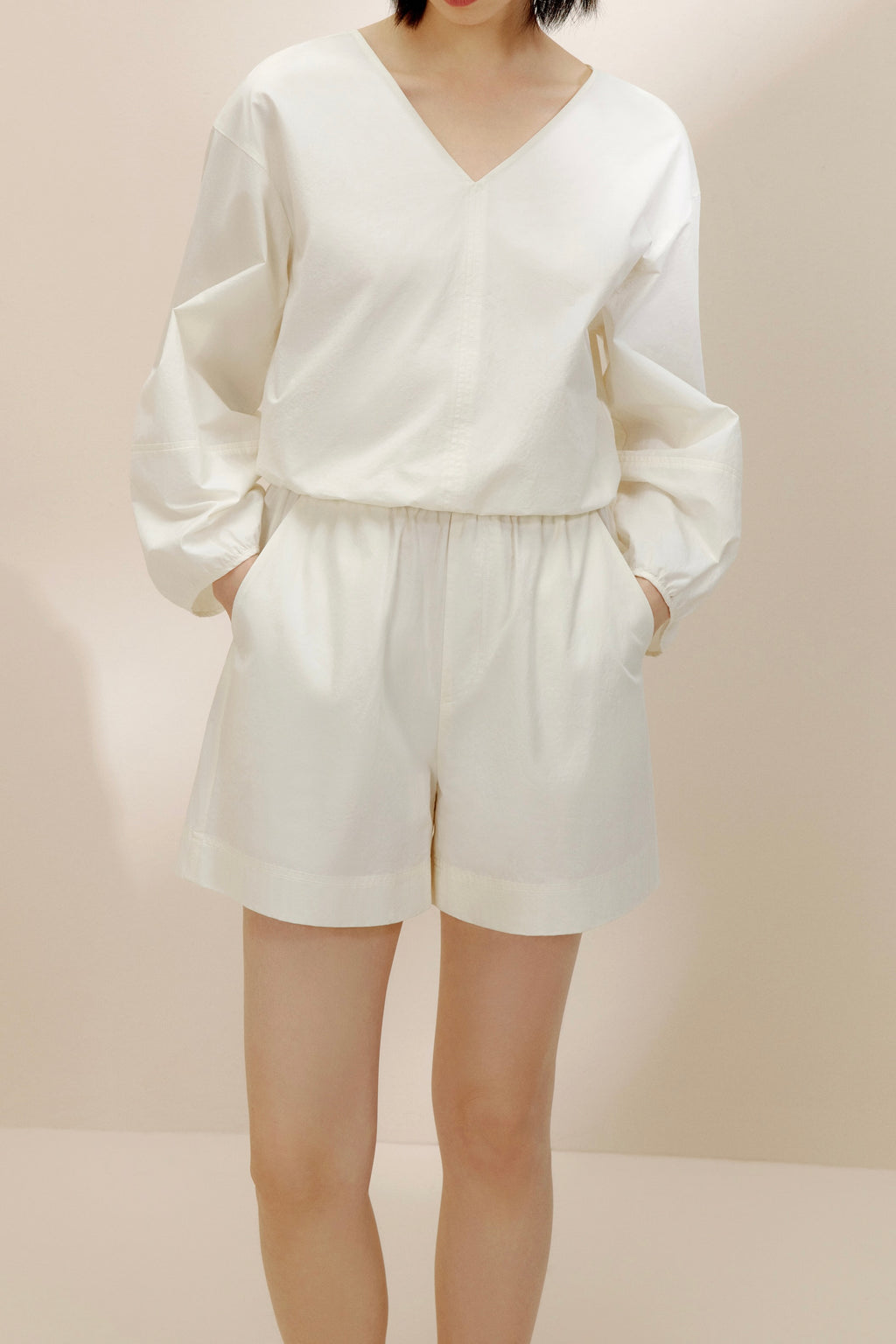 Woman wearing white long-sleeved top and white shorts.