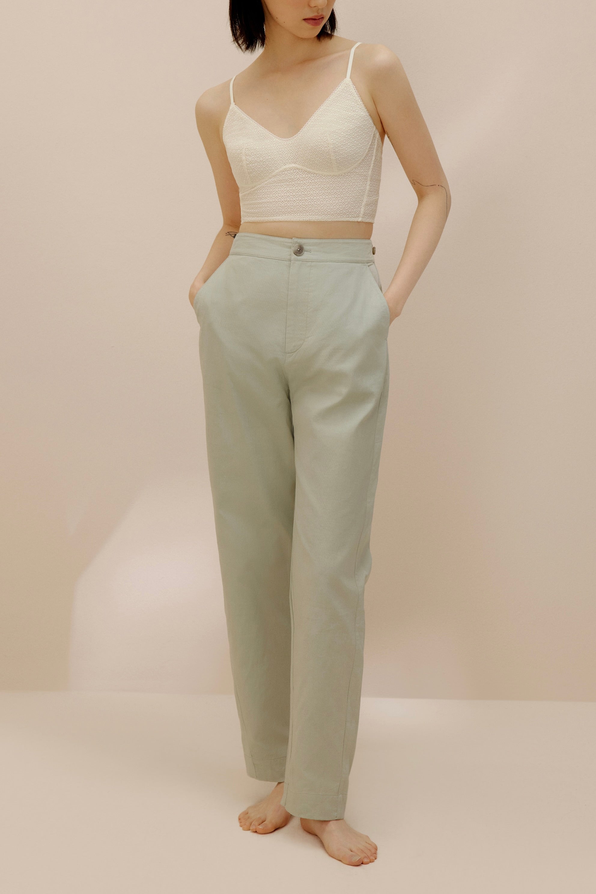 Front view of model wearing light green pants with cream bra top.