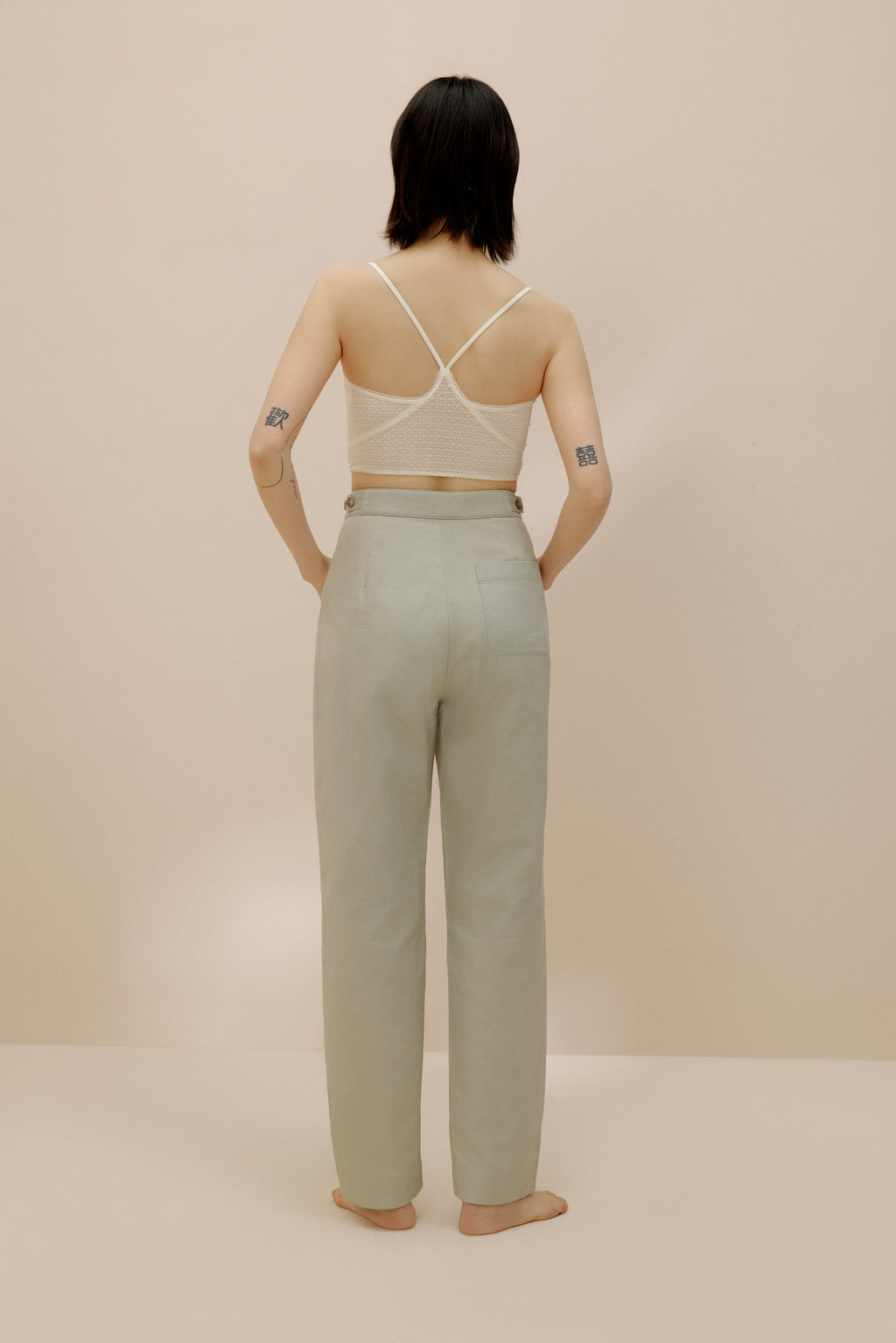 Back view of model wearing light green pants with cream bra top.