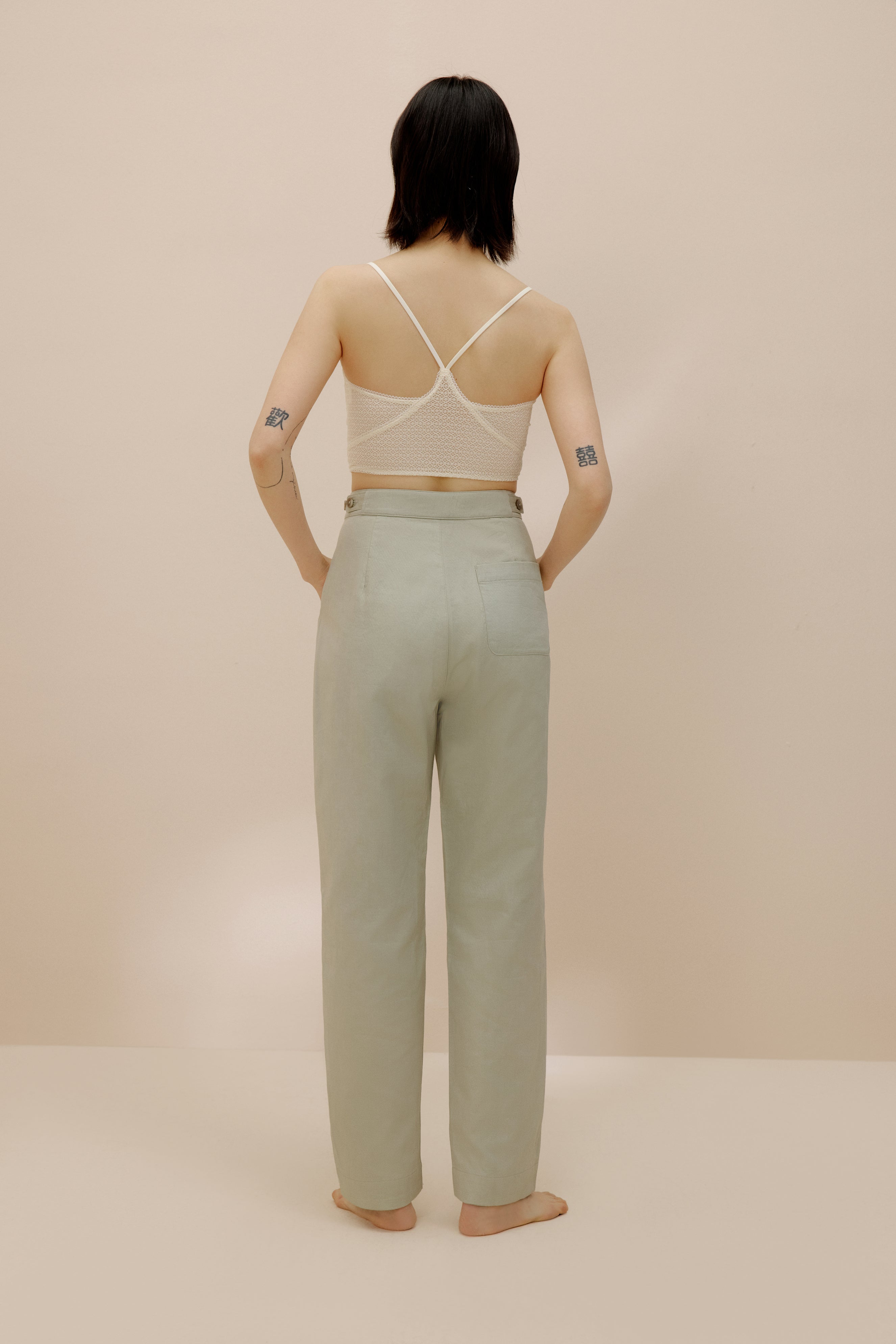 Back view of model wearing light green pants with cream bra top.