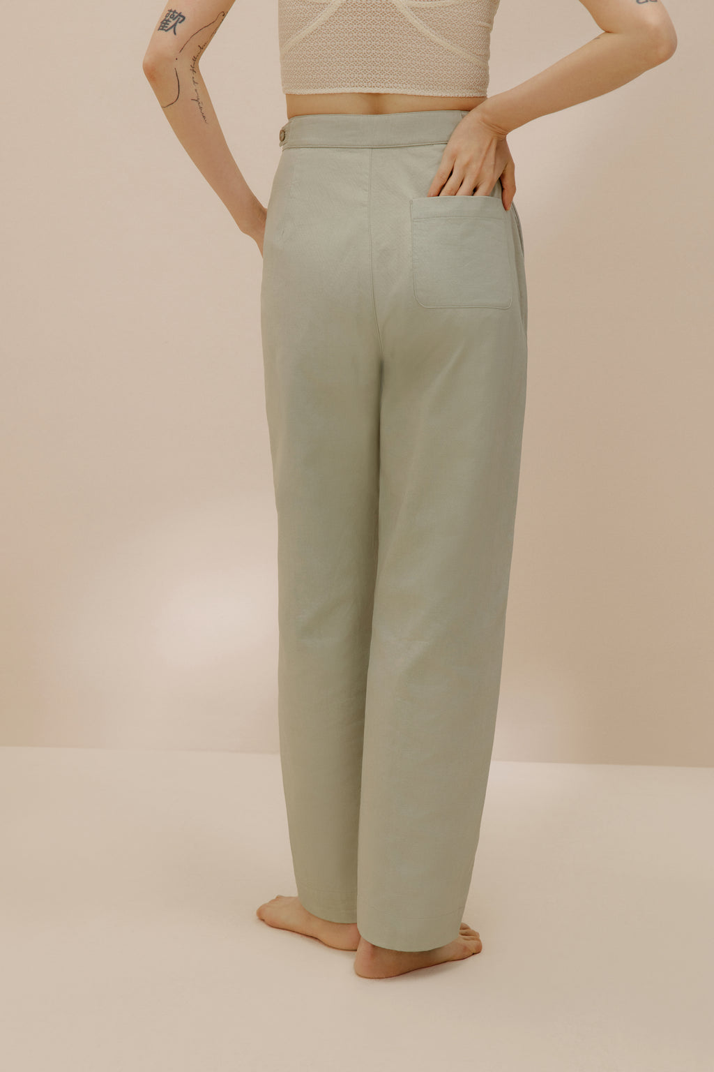 Back view of model putting her hand into back pocket of green pants.