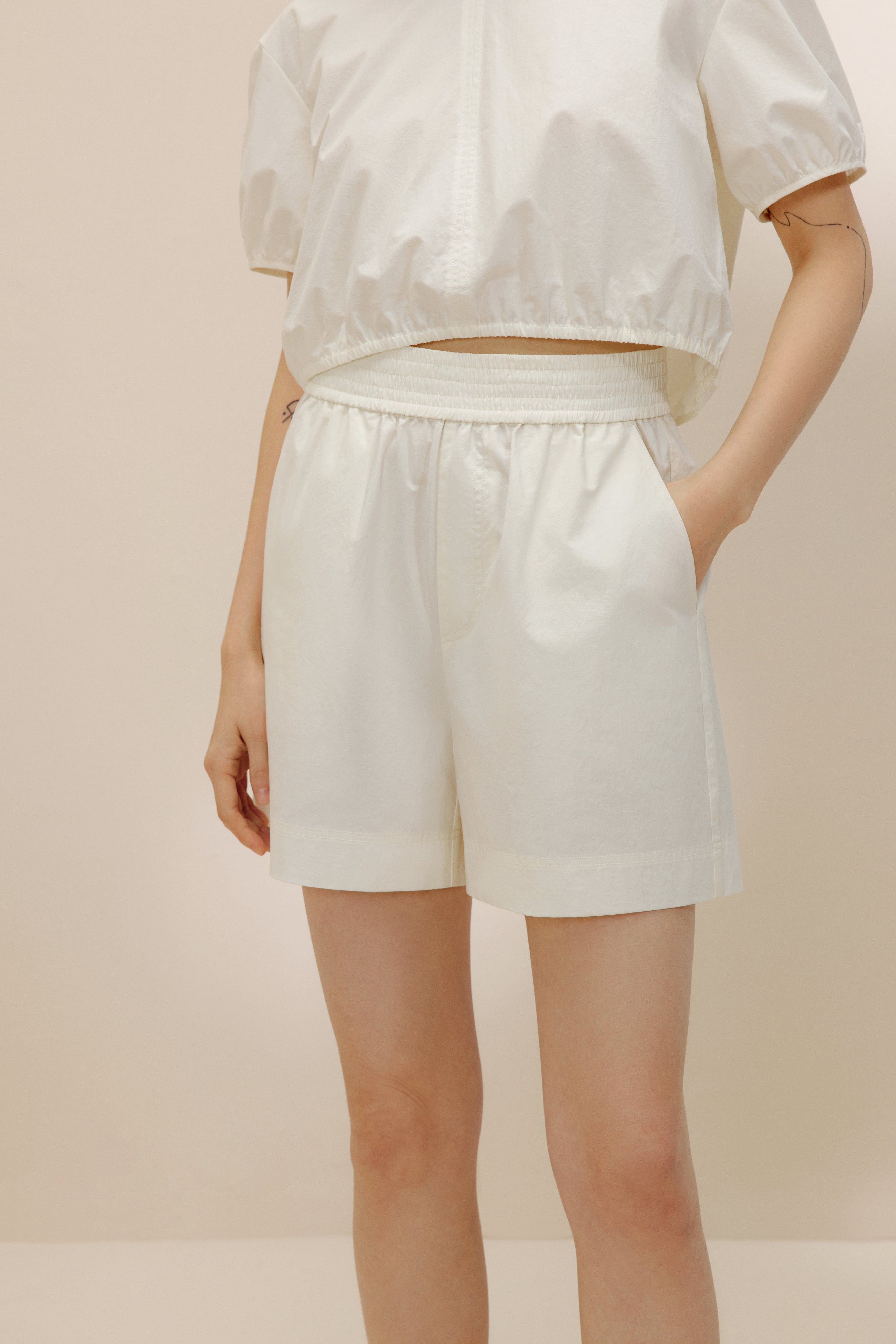 Front view of woman putting hand into pocket of white shorts.