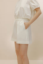 Side view of woman putting hand into pocket of white shorts.