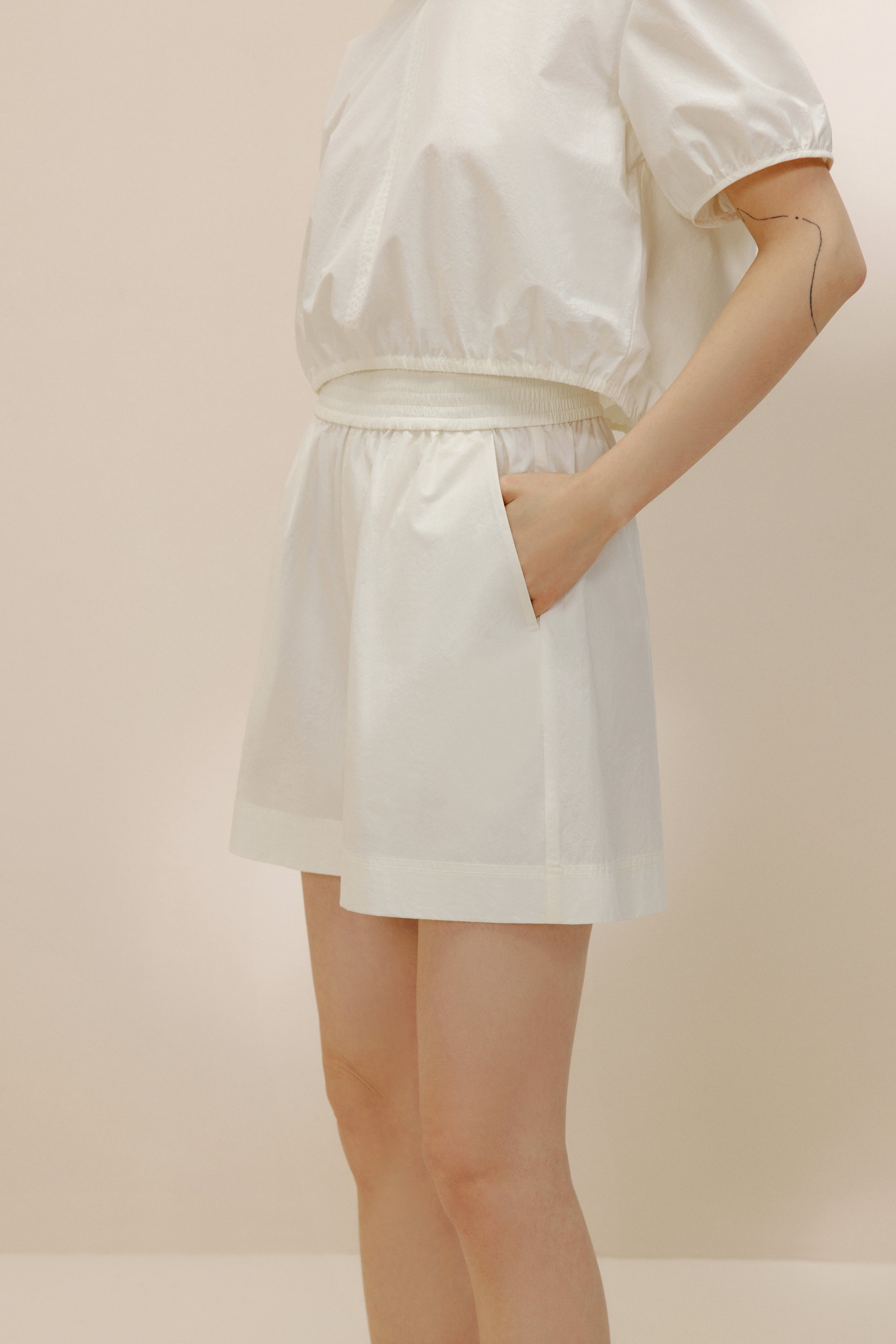 Side view of woman putting hand into pocket of white shorts.
