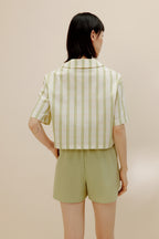 Back of woman wearing white and green short sleeved button up shirt and green pajama shorts