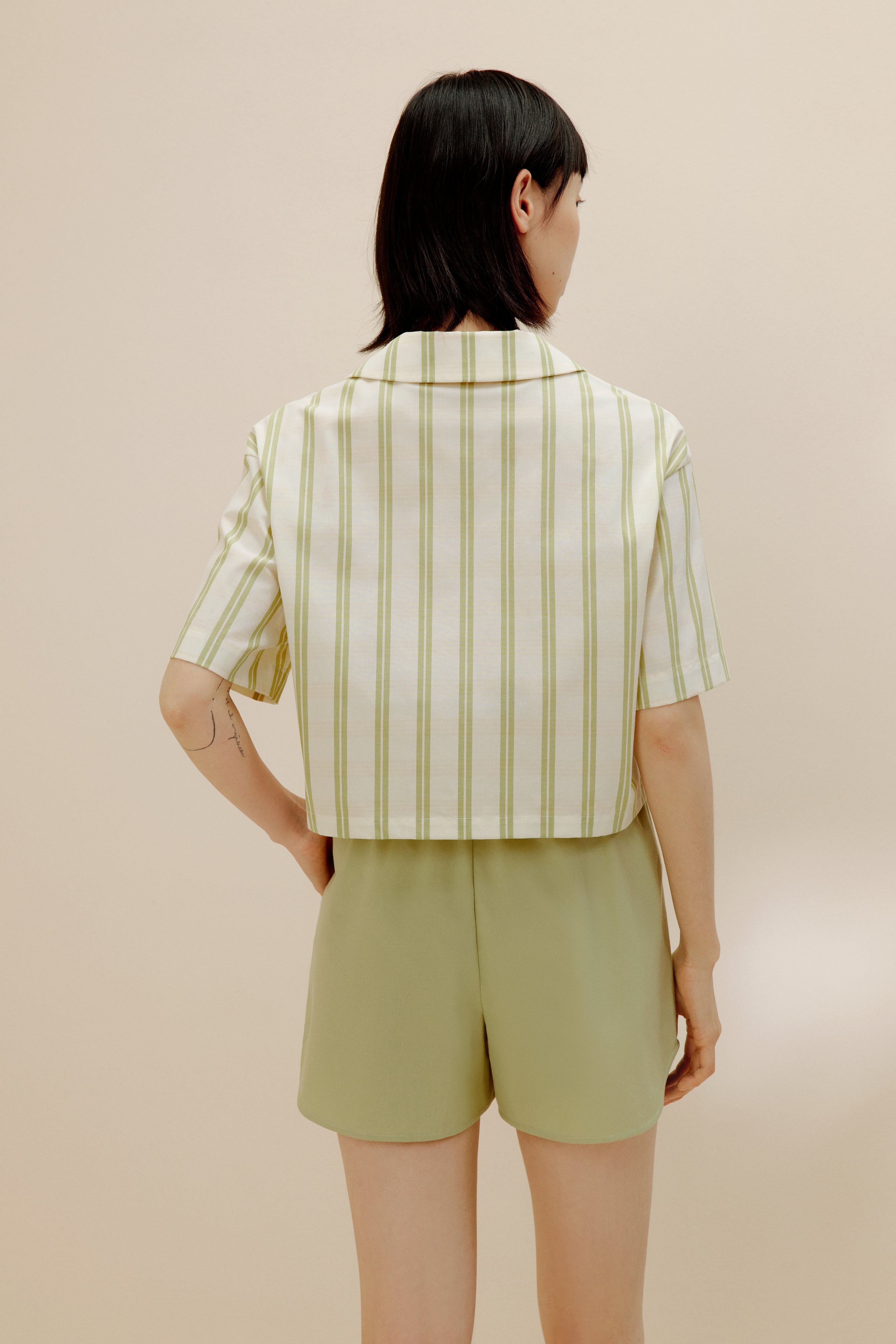 Back of woman wearing white and green short sleeved button up shirt and green pajama shorts