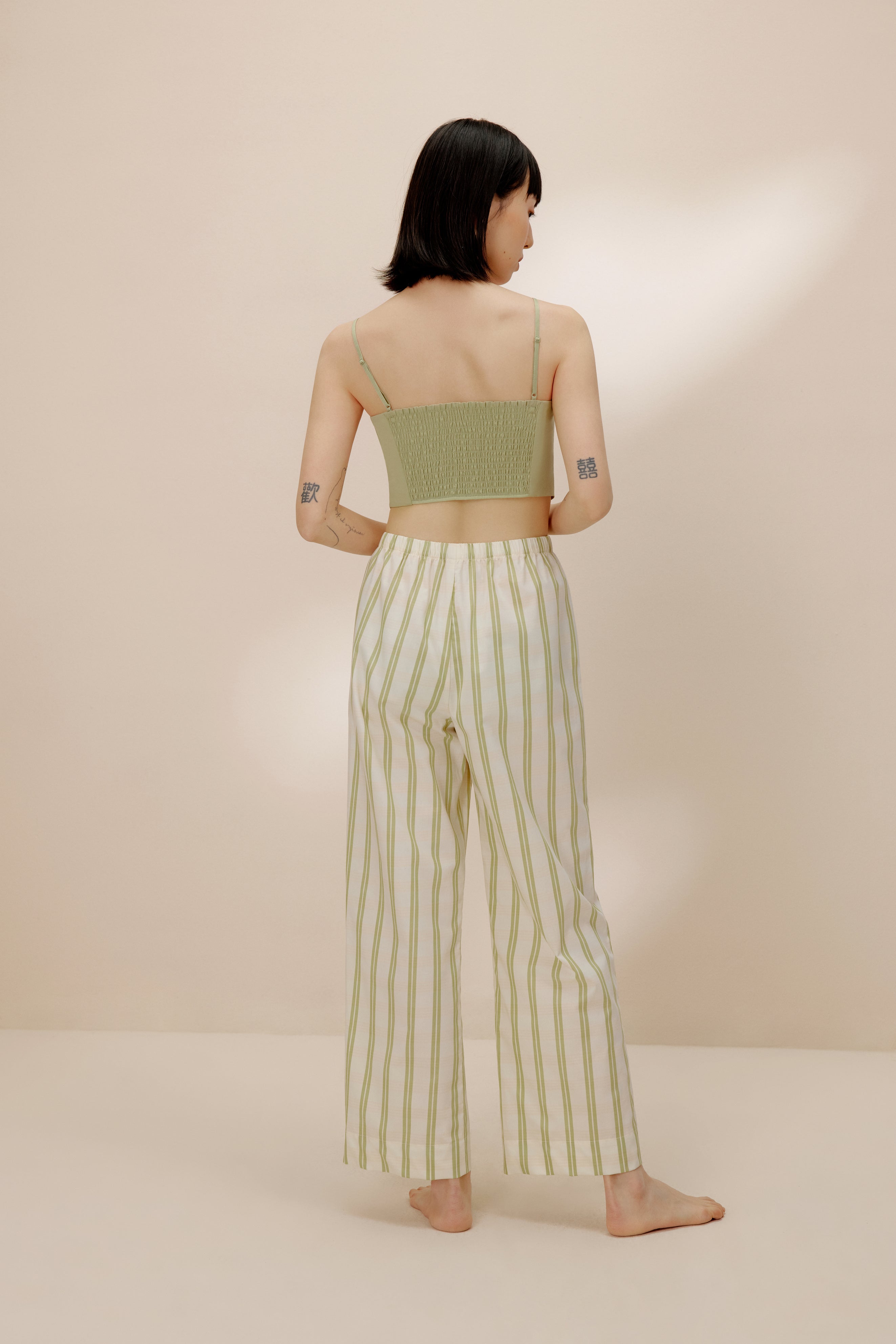 Back of woman wearing green tank top and white and green striped pajama pants