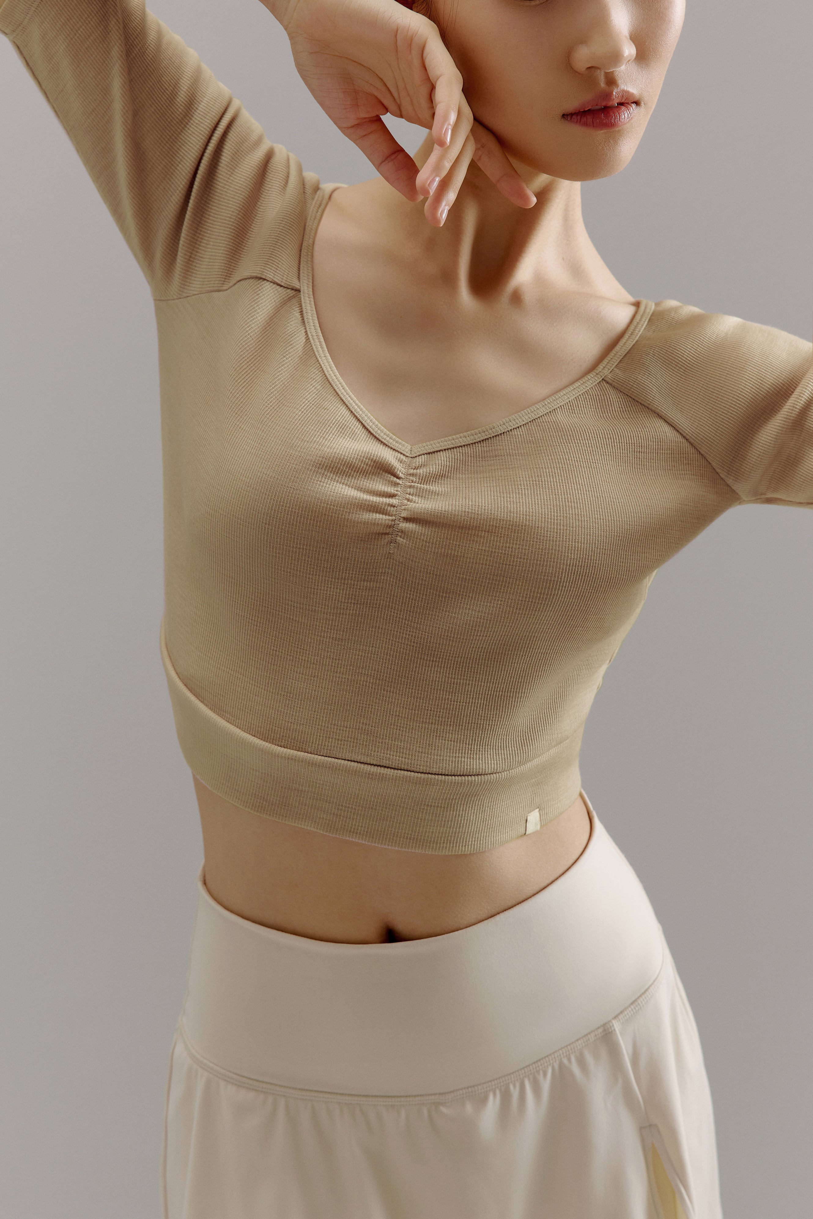 Front view of woman holding arm up wearing beige V-neck sweater.