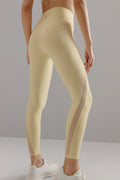 Bottom half of woman wearing yellow leggings with mesh overlay on side of legs
