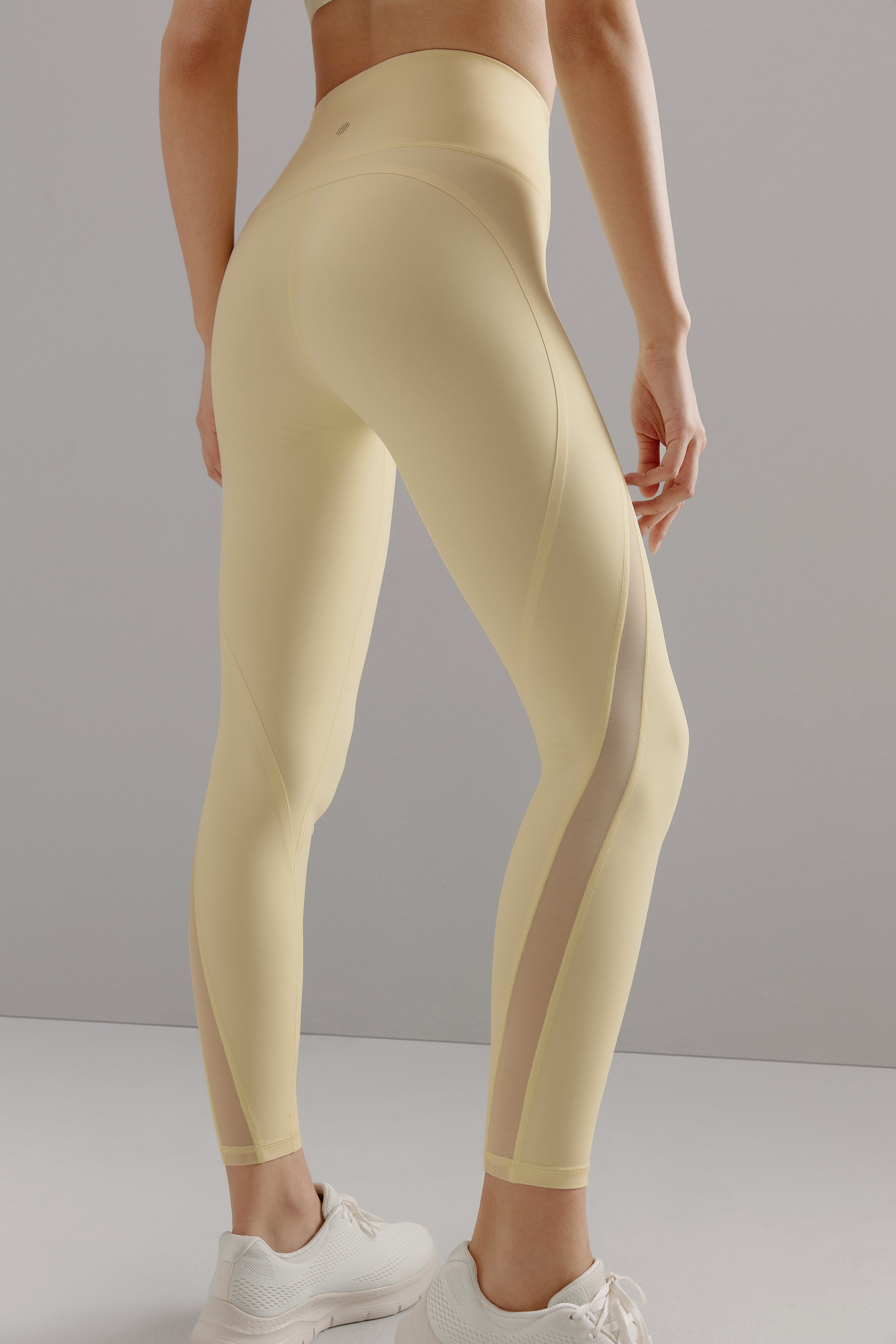 Bottom half of woman wearing yellow leggings with mesh overlay on side of legs