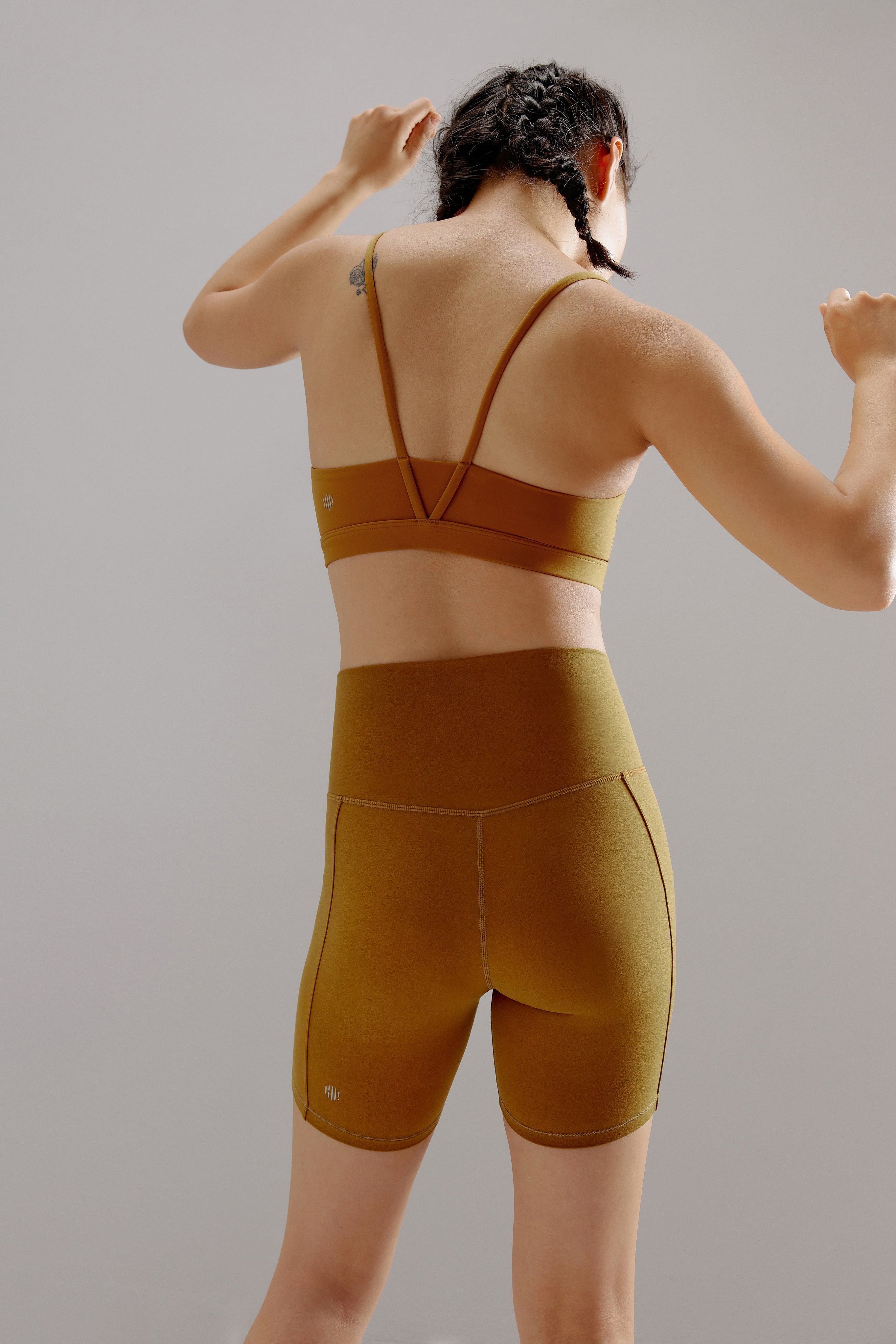 A woman wears a tan sports bra and shorts.