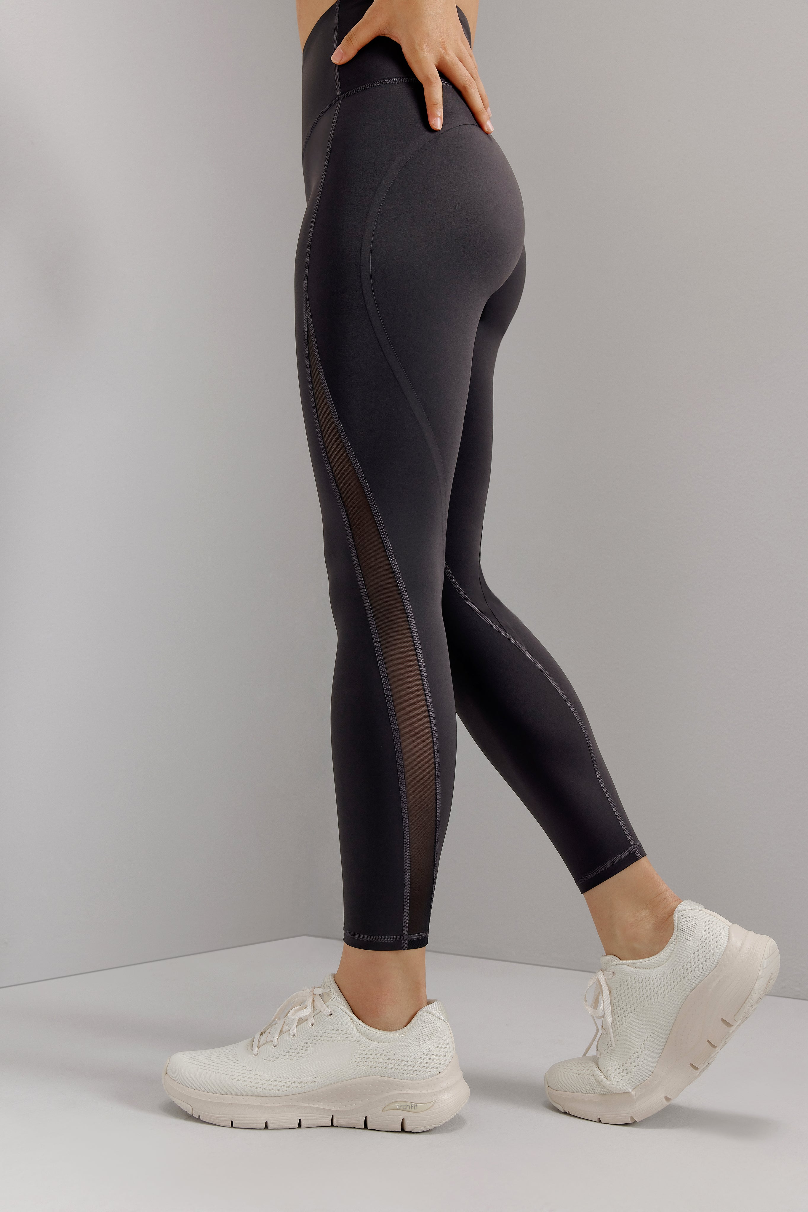 Bottom half of woman wearing black leggings with mesh overlay on side of legs