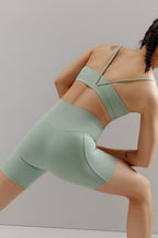 A woman wears a teal sports bra and shorts.