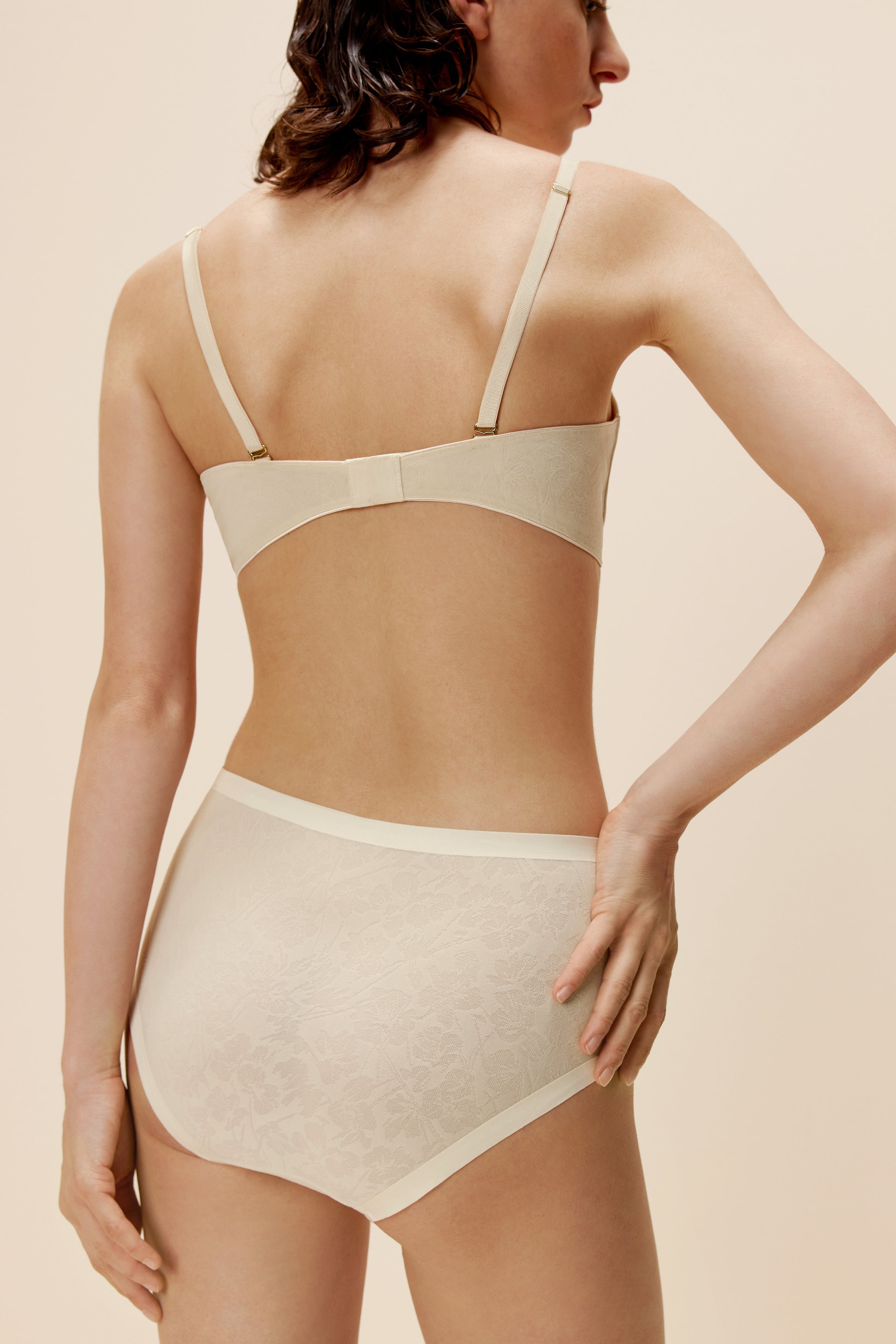 Back of woman wearing off-white lace bra and matching briefs