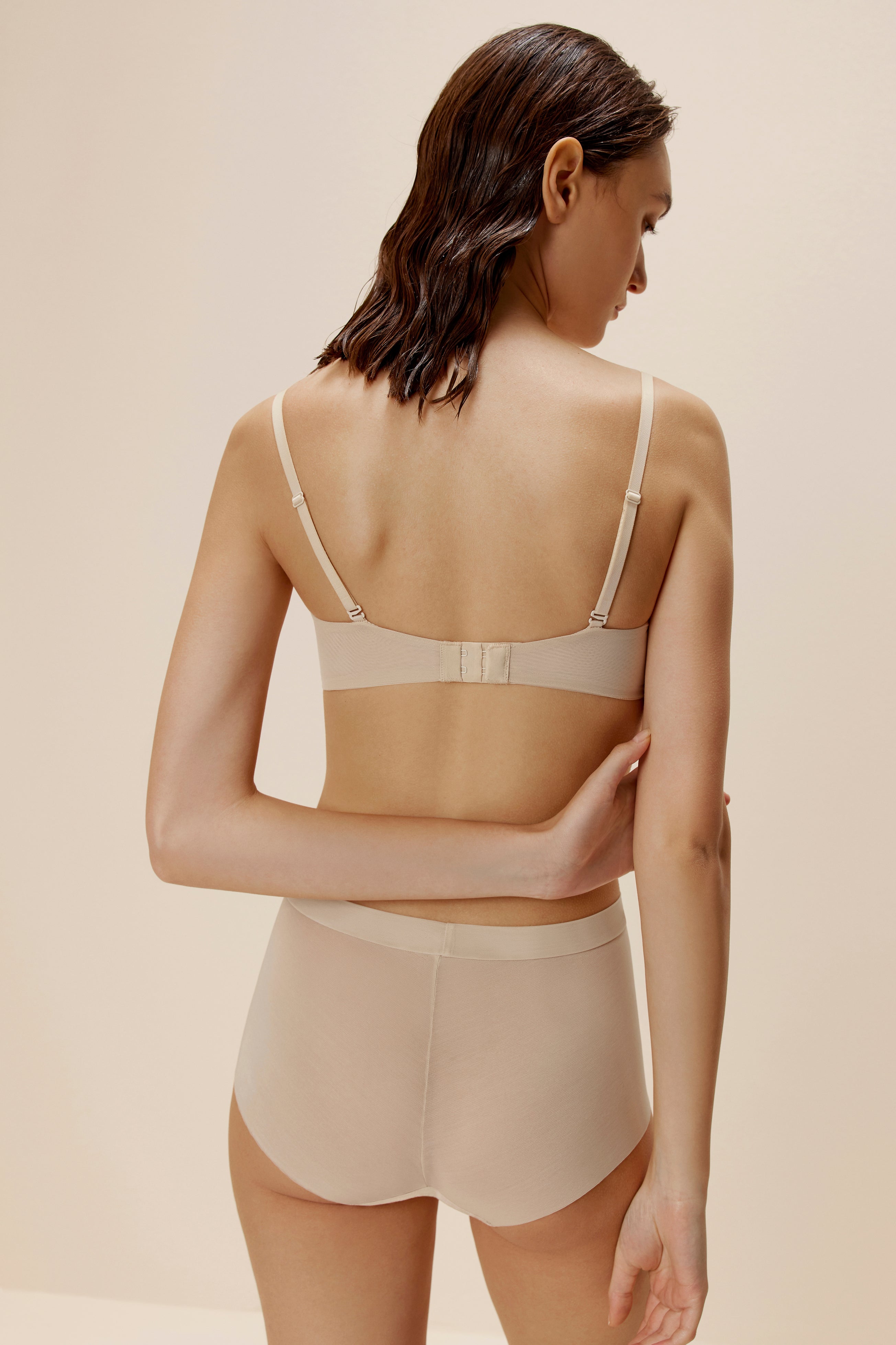 Back of woman wearing beige high waisted mesh briefs and matching bra
