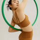 woman wearing a yellow sports bra and leggings, holding a hula hoop