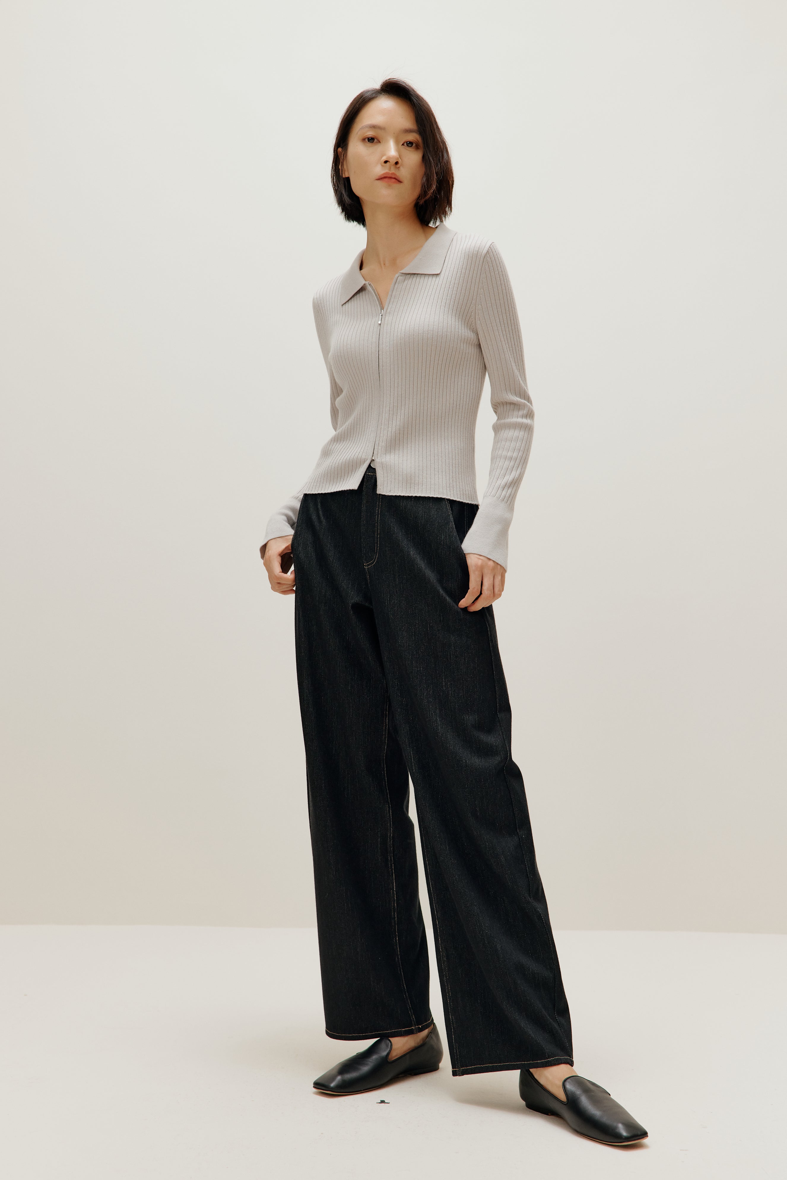 A woman wears a gray silky wool zip-up cardigan, black pants, and black shoes.