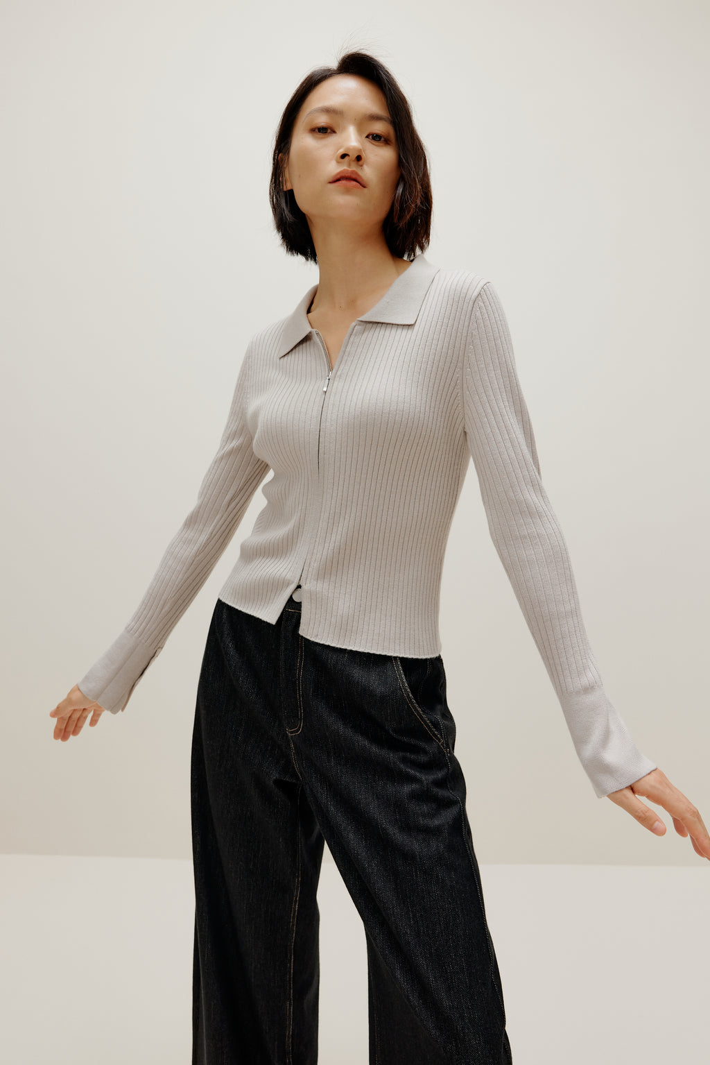 A woman wears a gray silky wool zip-up cardigan and black pants.