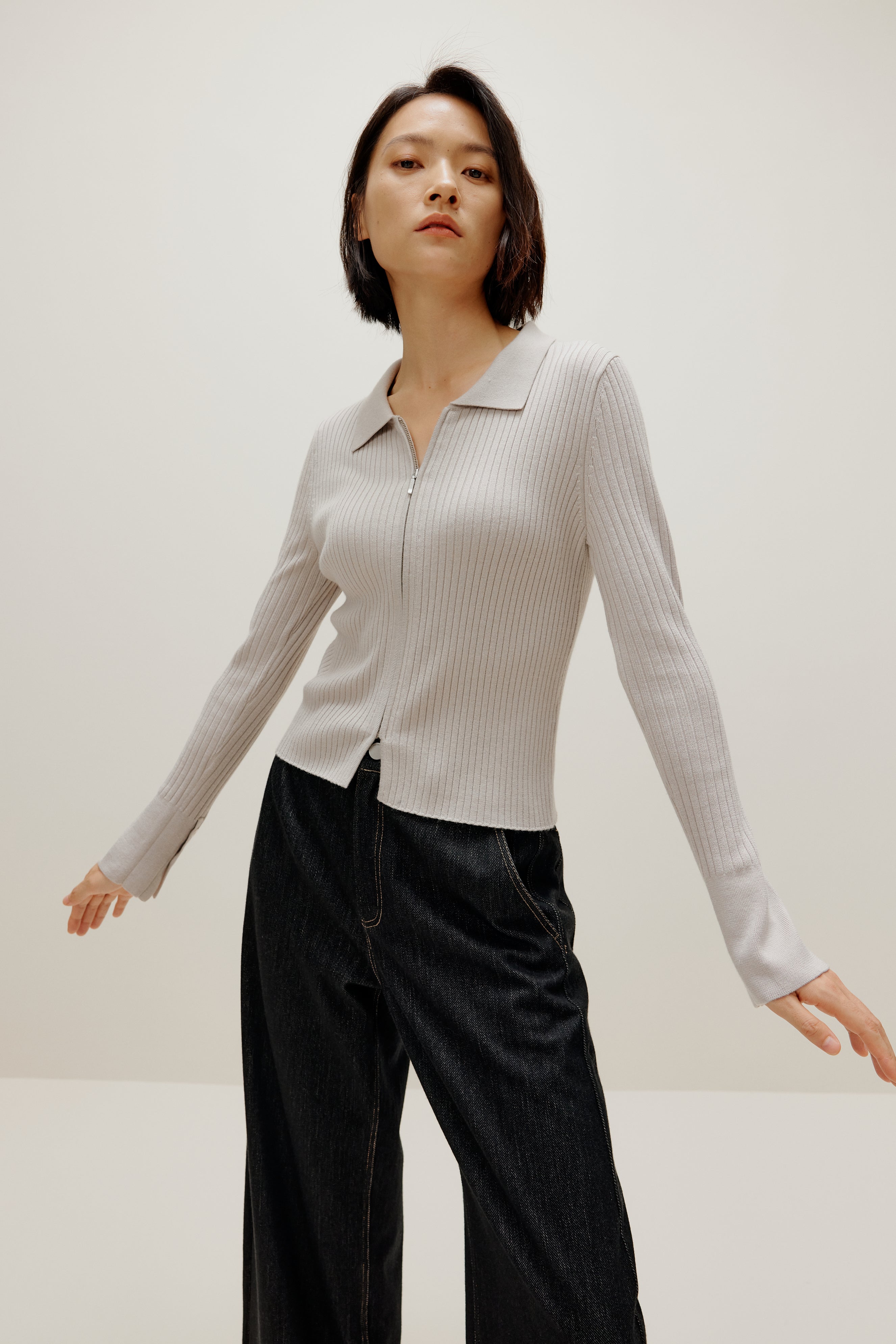 A woman wears a gray silky wool zip-up cardigan and black pants.