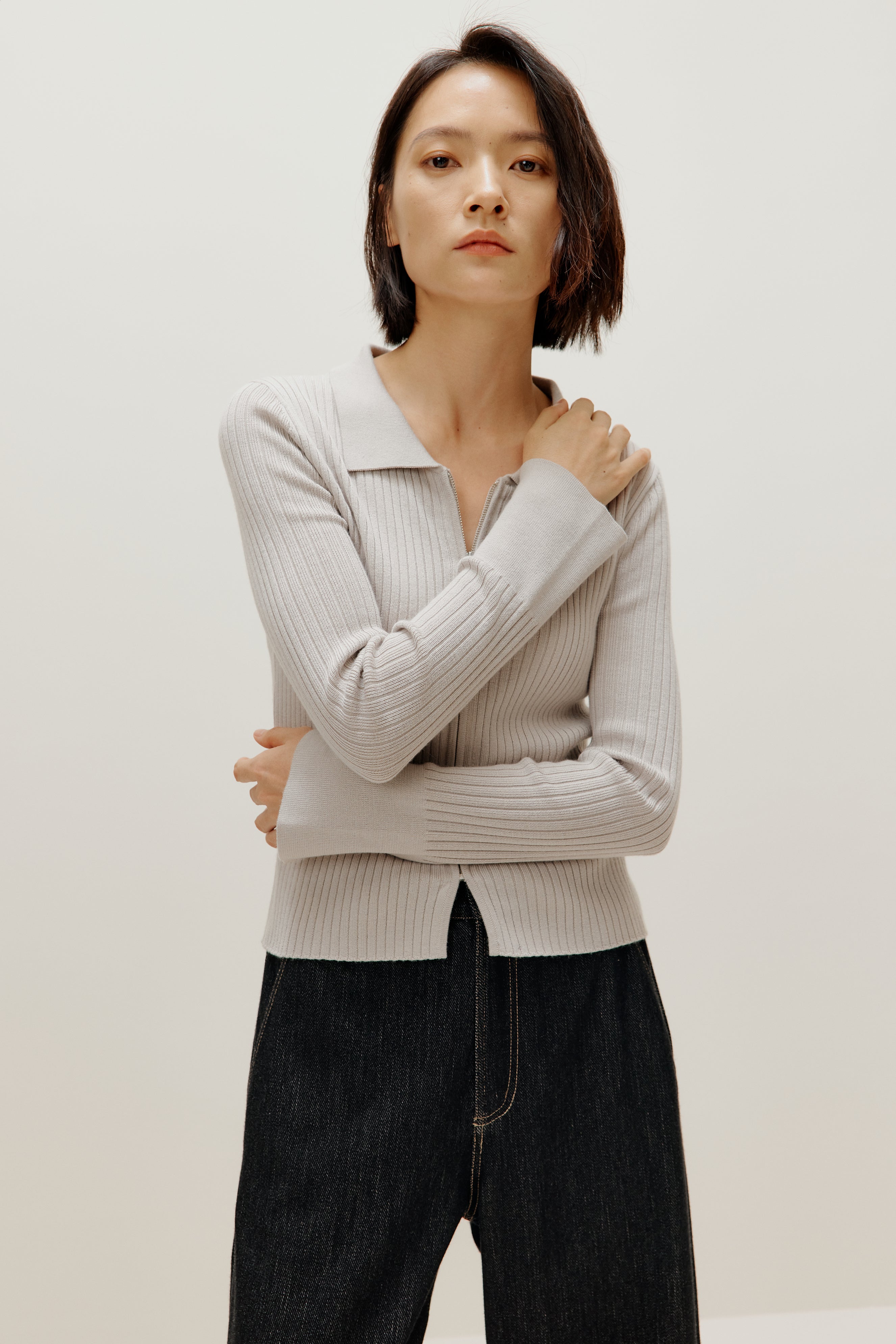 A woman wears a gray silky wool zip-up cardigan and black pants.